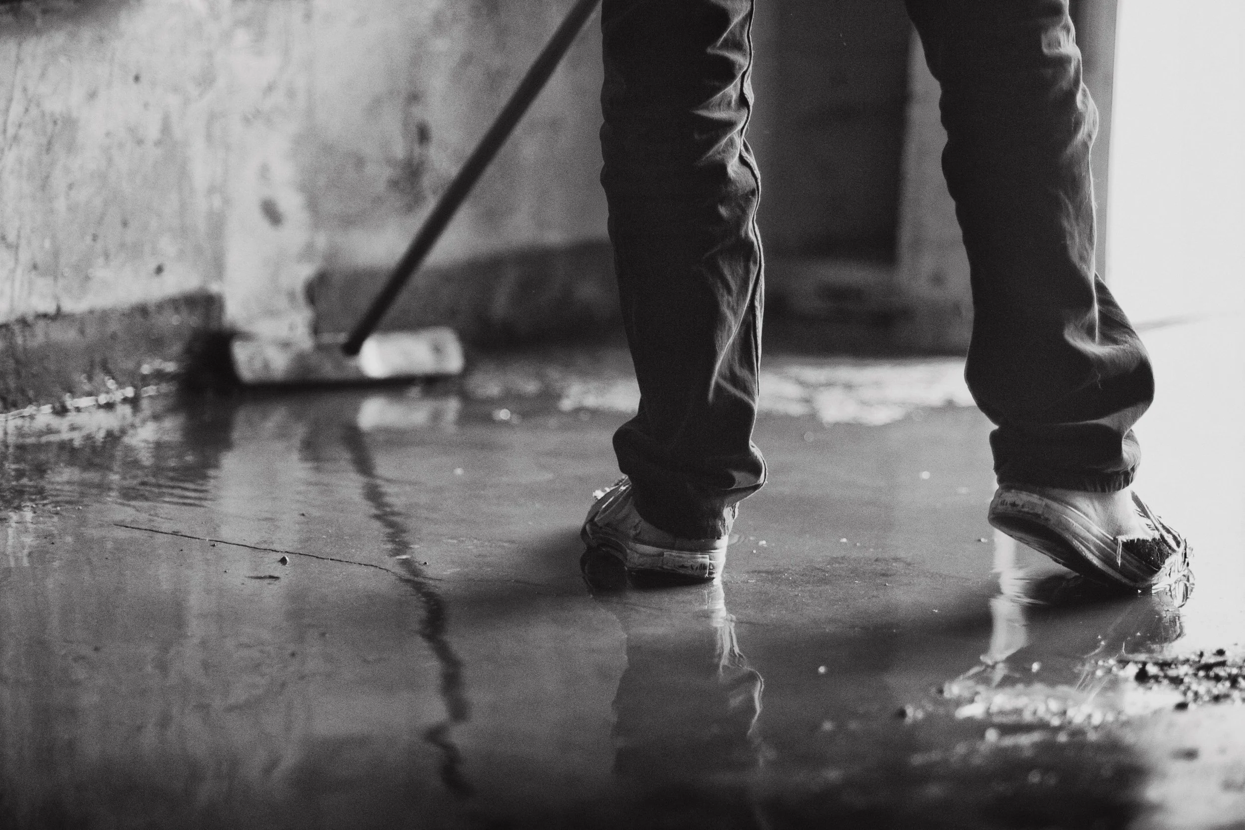 Person beim Fliesenlegen, die nassen Fliesen auf der Bodenfläche auflegt, in schwarz-weiß aufgenommen.