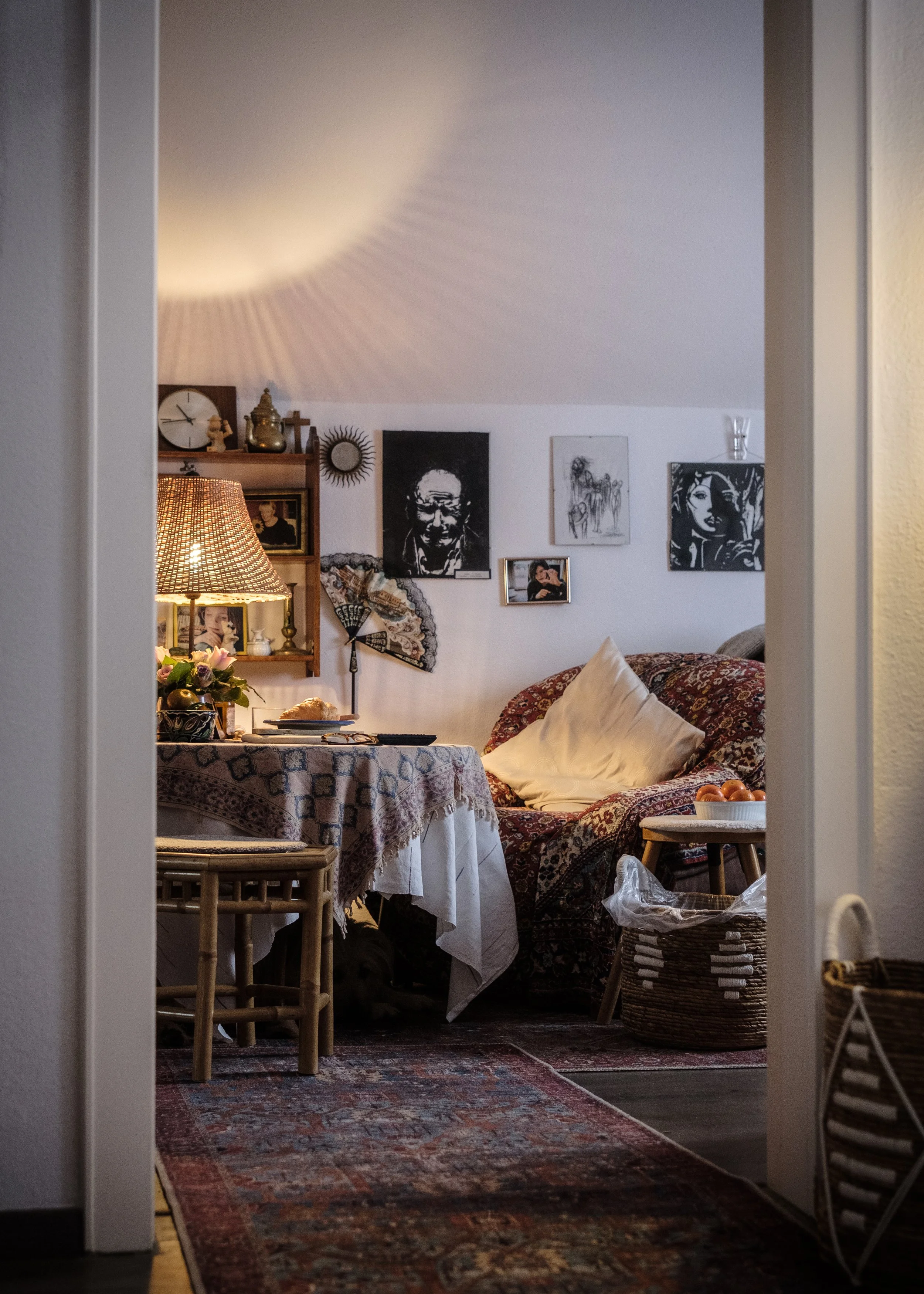 Gemütliches Wohnzimmer mit vintage Dekor, einem bunten Teppich, einem Sofa mit Kissen, Wandbildern und Lampen, die warmes Licht spenden.