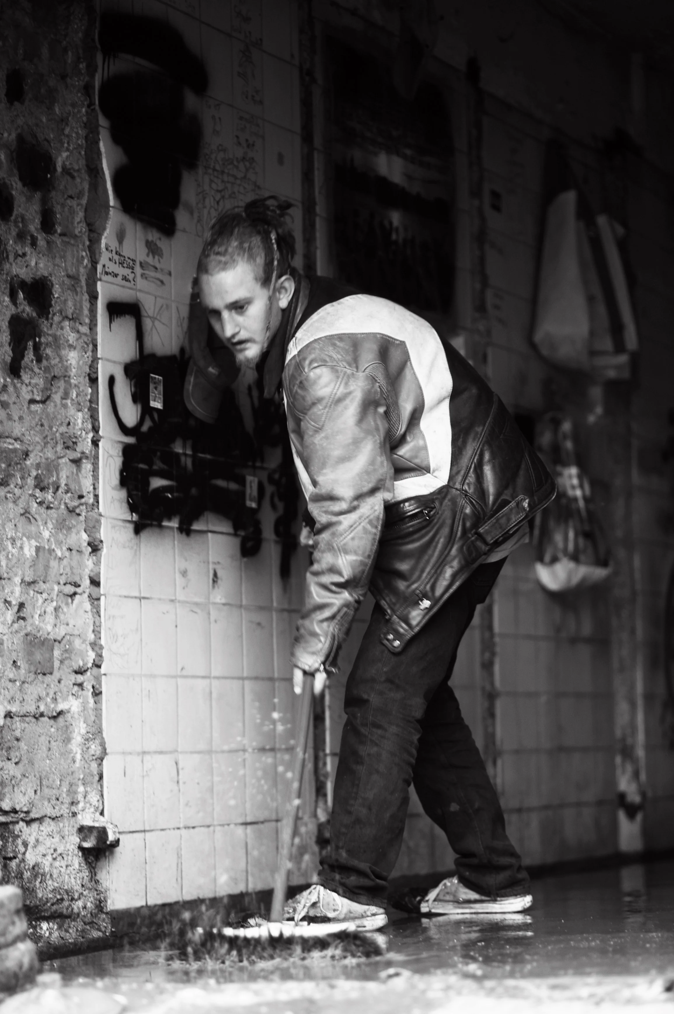 Ein junger Mann mit einem Piraten-Tattoo auf seinem Kopf putzt den Boden in einem dunklen, urbanen Raum.