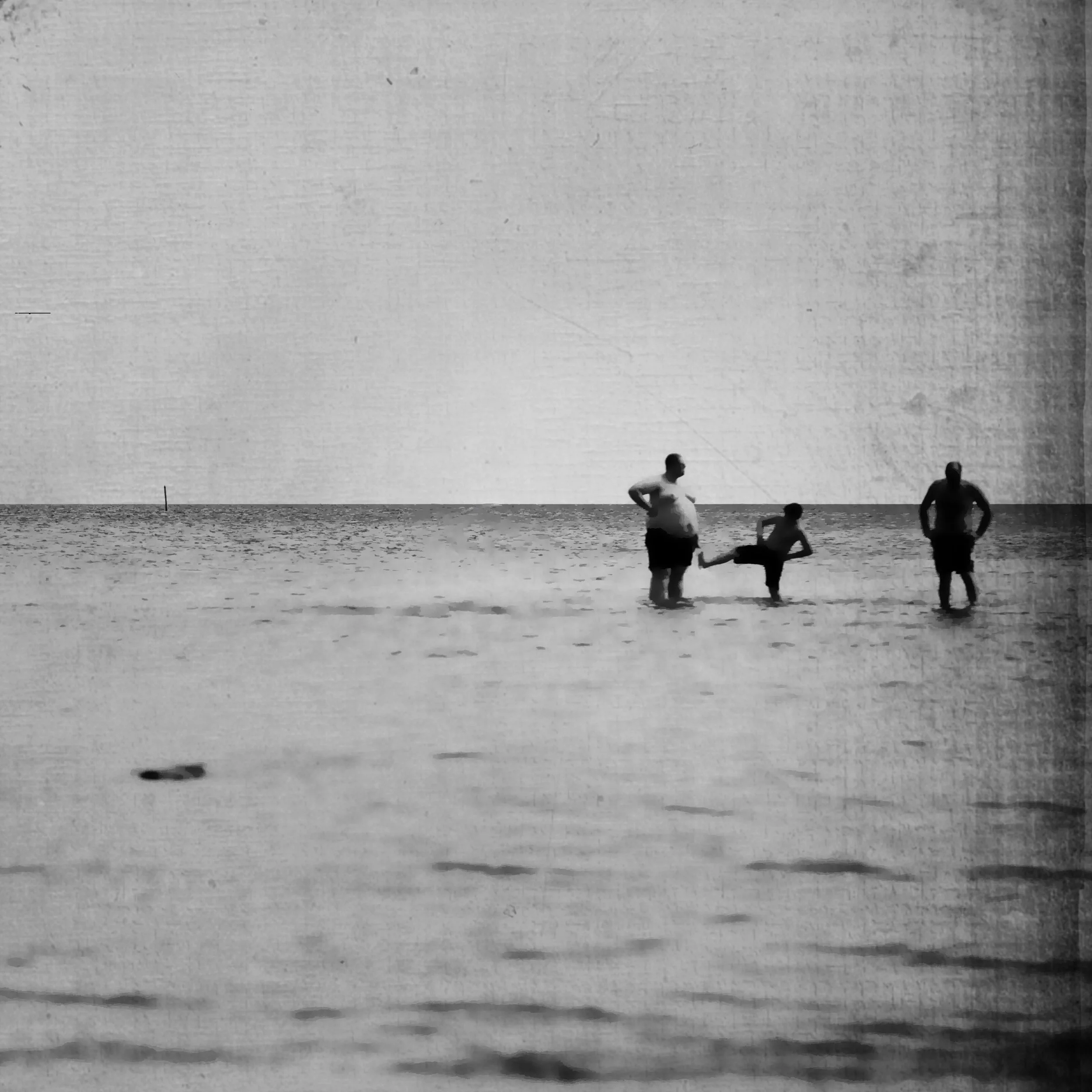 Schwarz-weiß Bild von drei Personen im Wasser am Strand, eine Erwachsene und zwei Kinder.