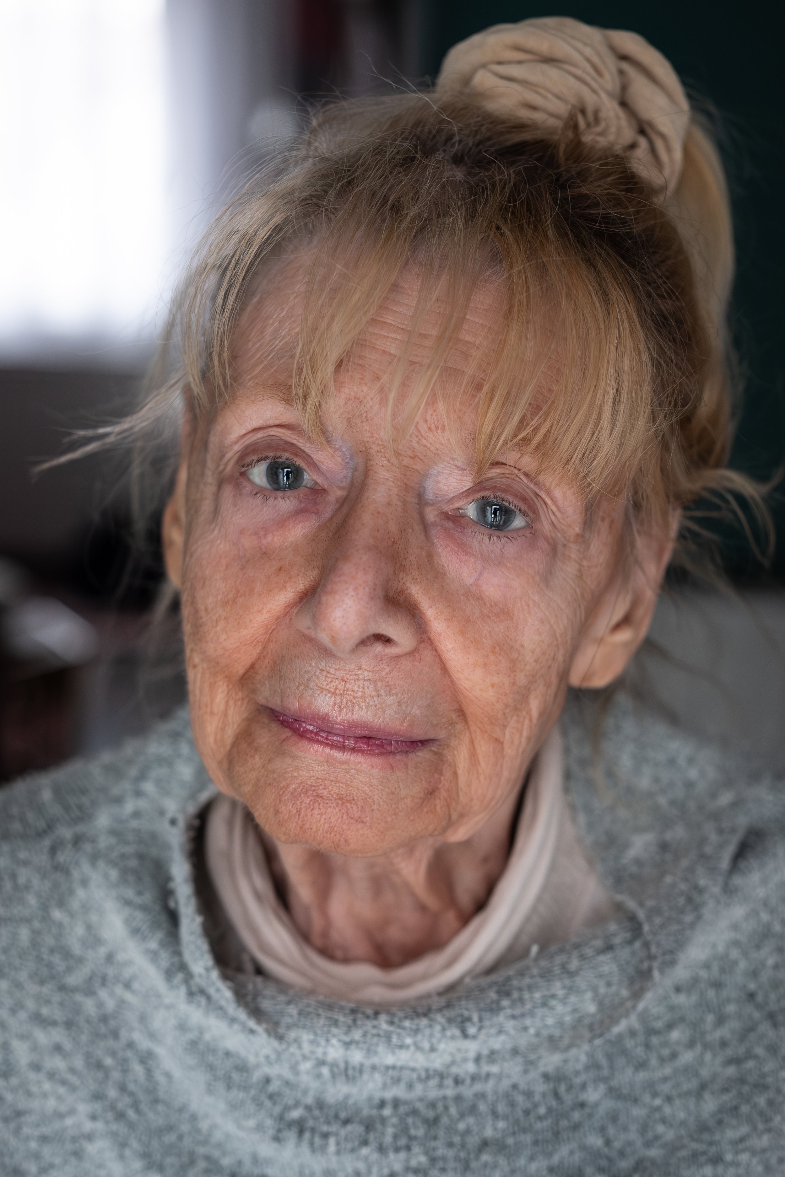 Nahaufnahme eines älteren Mädchens mit blonden Haaren, blauen Augen und einem grauen Pullover