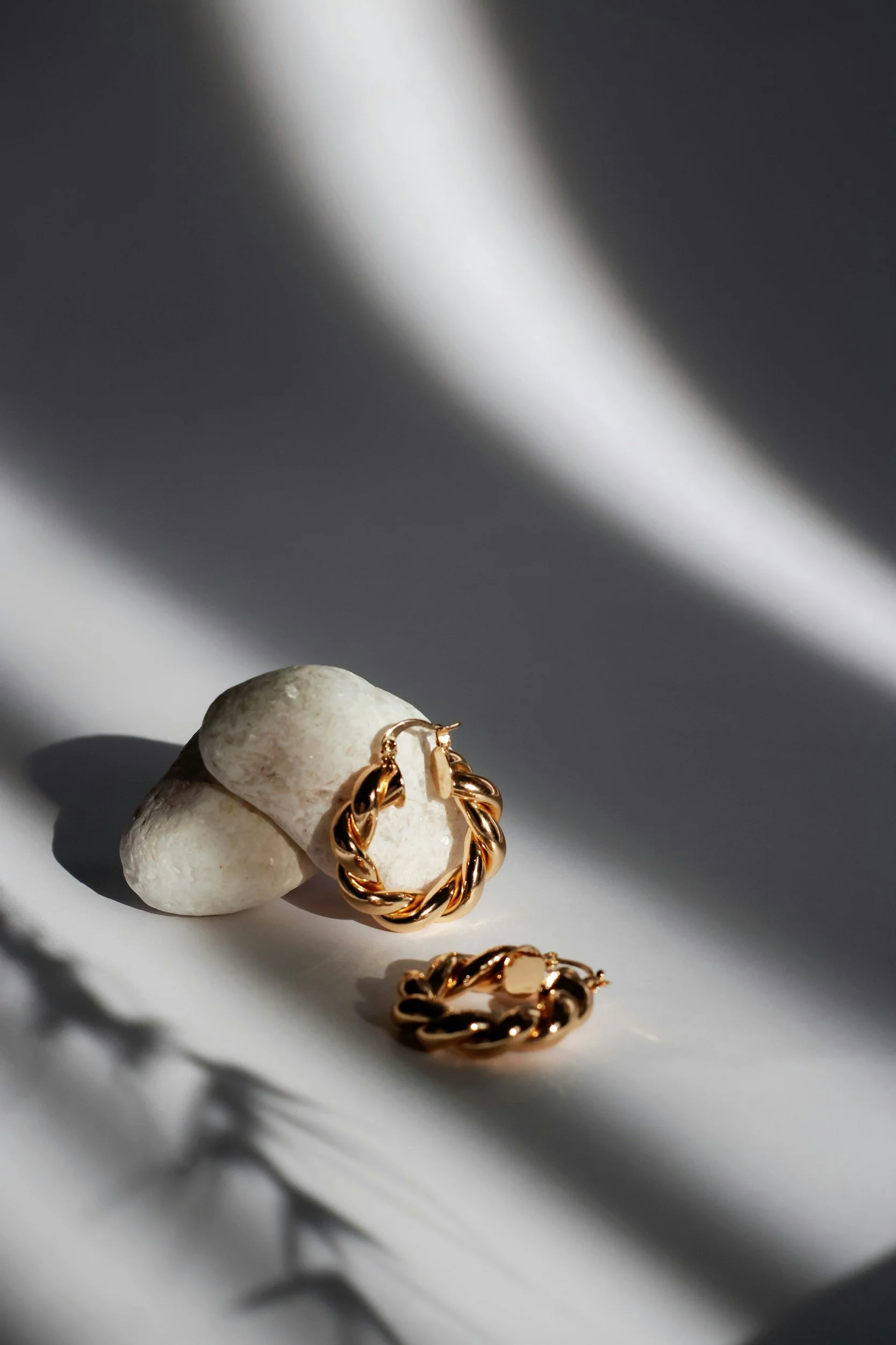 Close-up of gold twisted hoop earrings on a white stone with shadows and light reflections