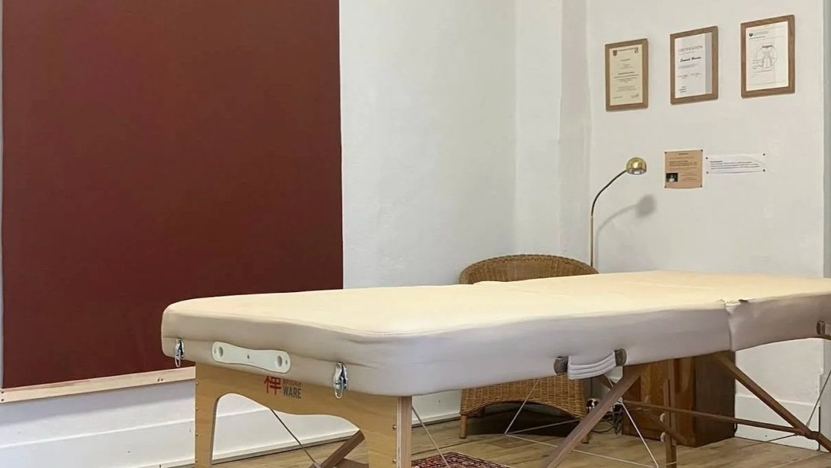 Behandlungsraum mit Behandlungsliege, Wand mit Diplomen und einem Leselicht.