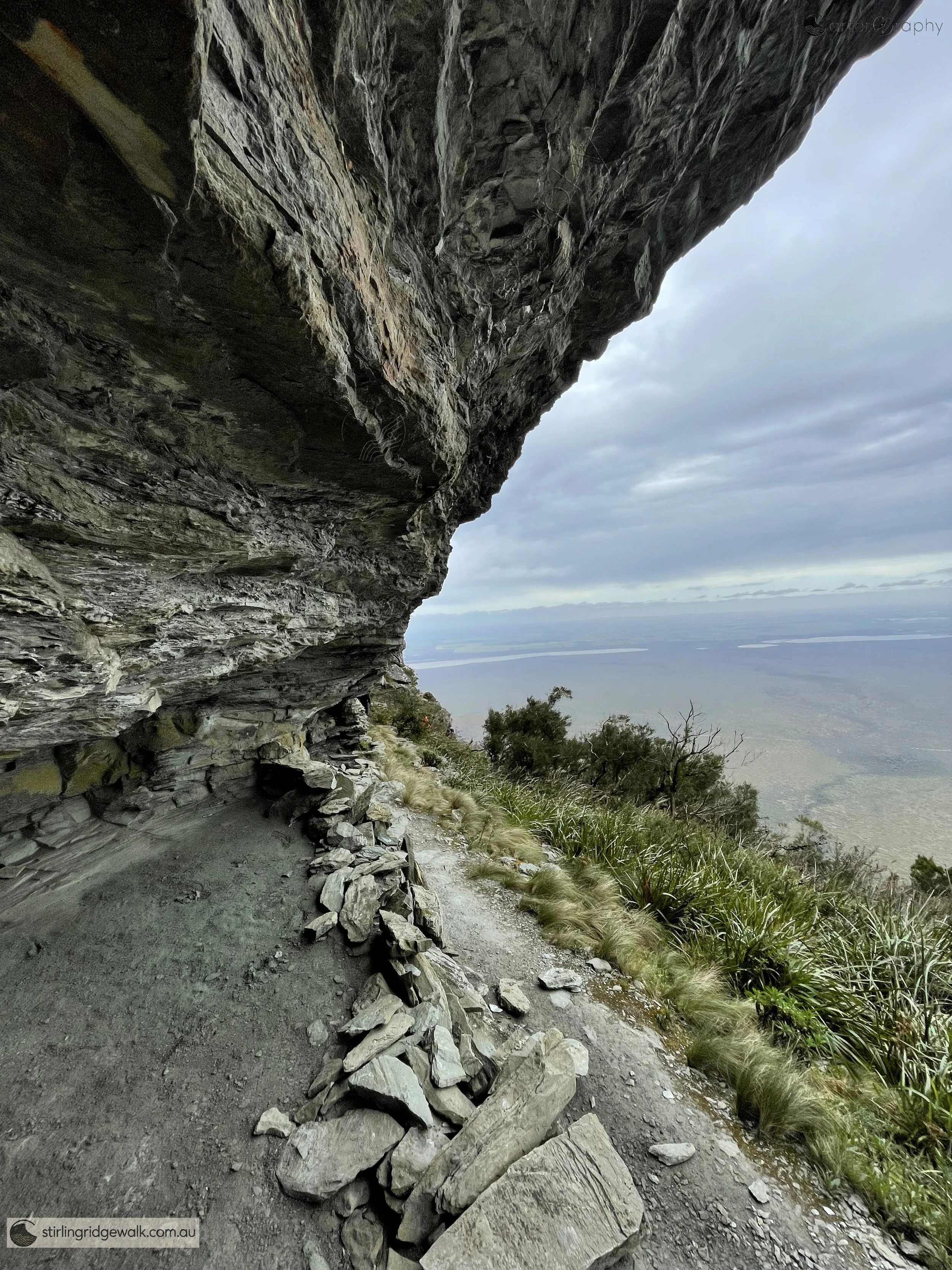 A small camping cave beneath a rock overhang on the southern traverse of Pyungoorup Peak, with expansive views across the plains to the south.
