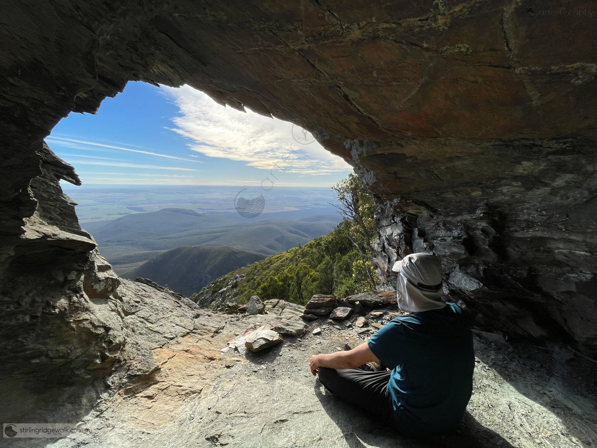 Ellen Peak Cave, a small rock shelter tucked beneath the northern base of Ellen Peak just off the track, with enough sheltered space for perhaps two people. The opening looks north across the lower plains with Moir Hill visible.