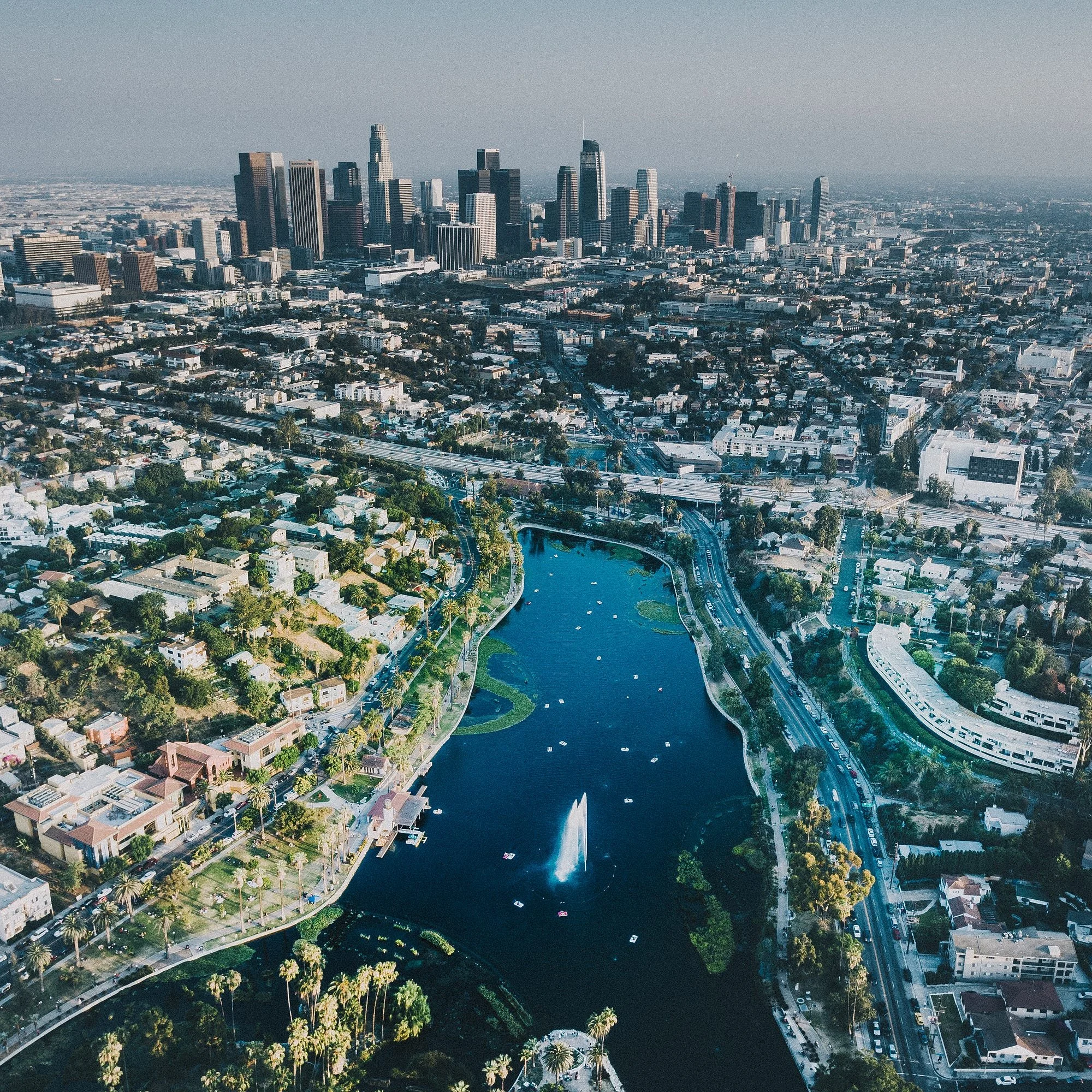 An aerial view of a city with skyscrapers, a river with boats, and roads, likely Los Angeles.