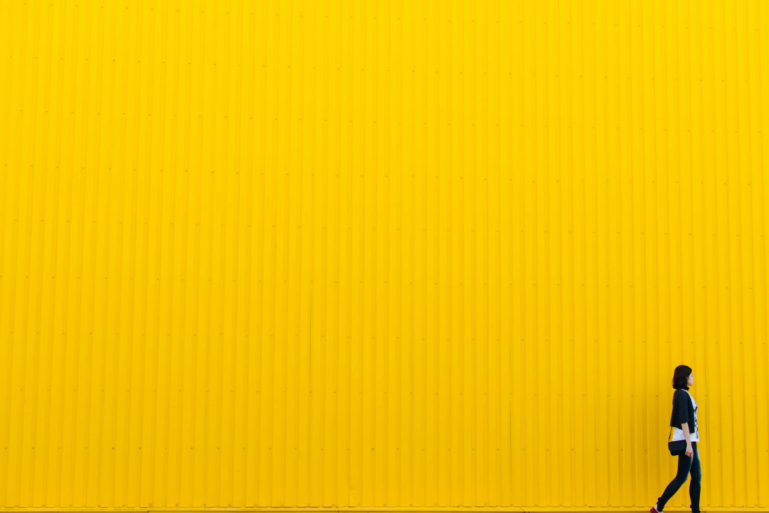 A woman walking past a large yellow corrugated metal wall.