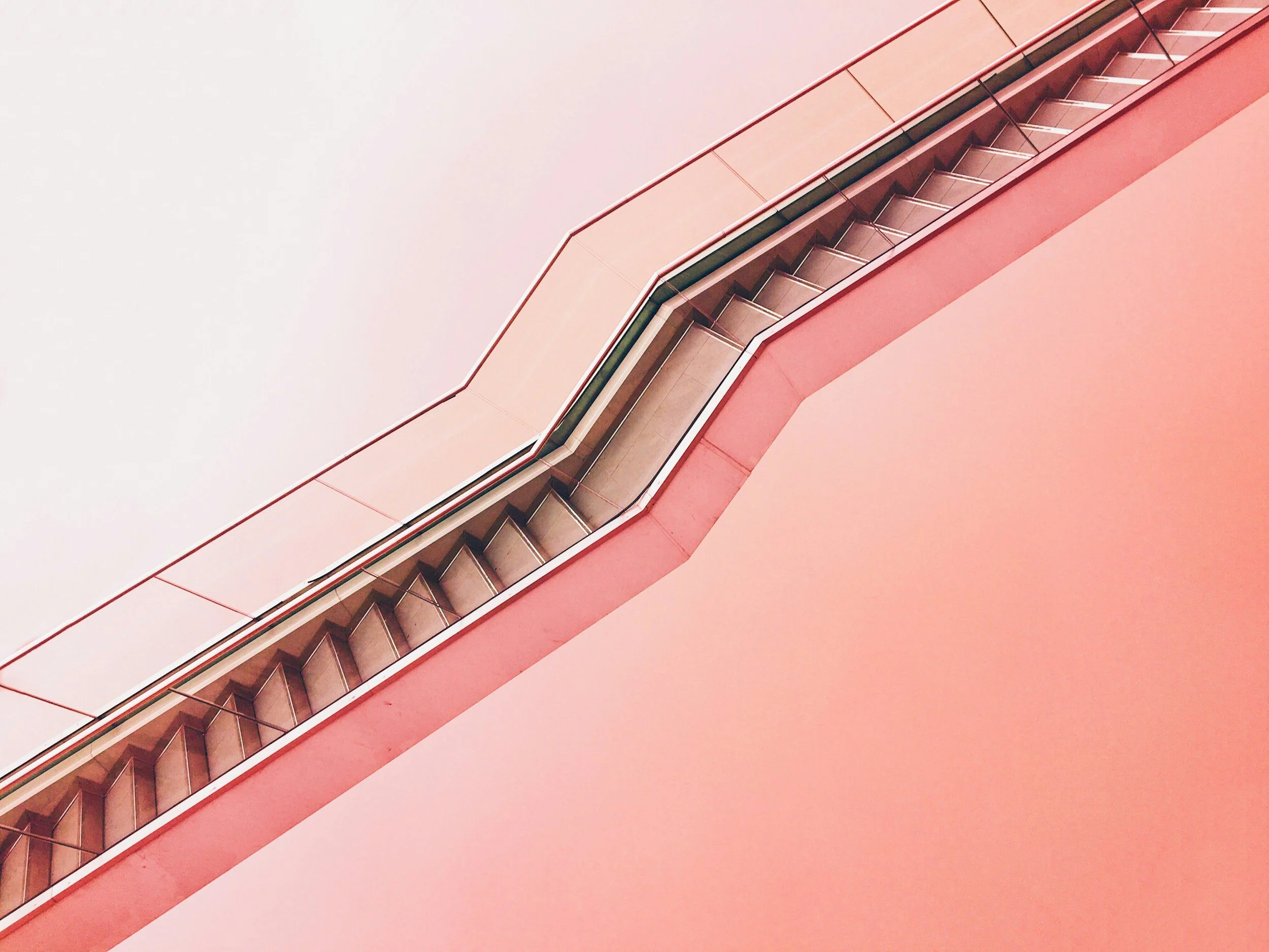 Close-up of pink staircase with metal handrails, viewed from below against a plain wall.