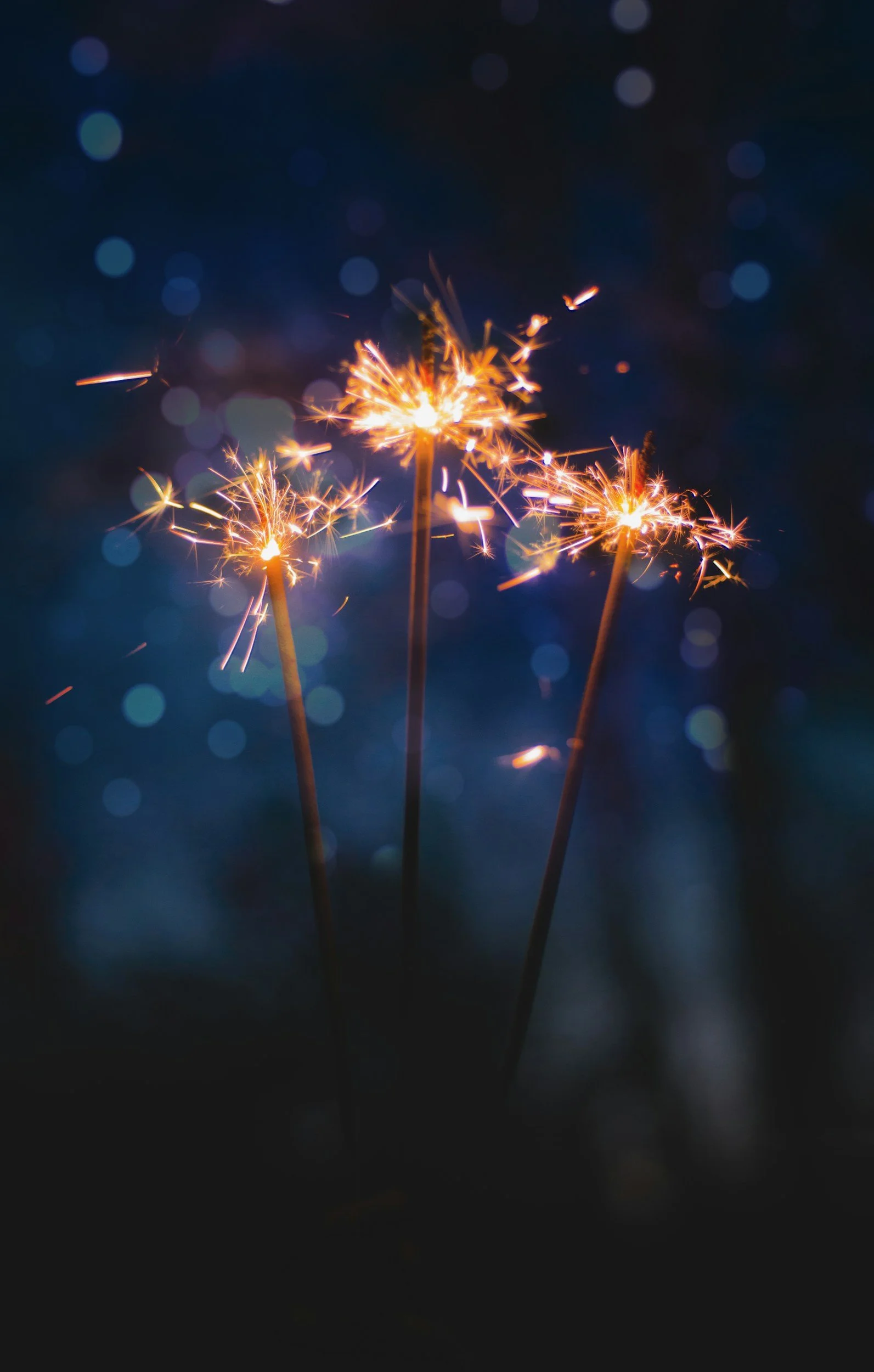 Three sparklers lit against a dark background with blurred blue lights.