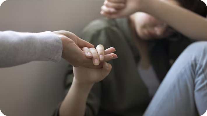 A person holding hands with another person who appears distressed, with the second person covering their face.