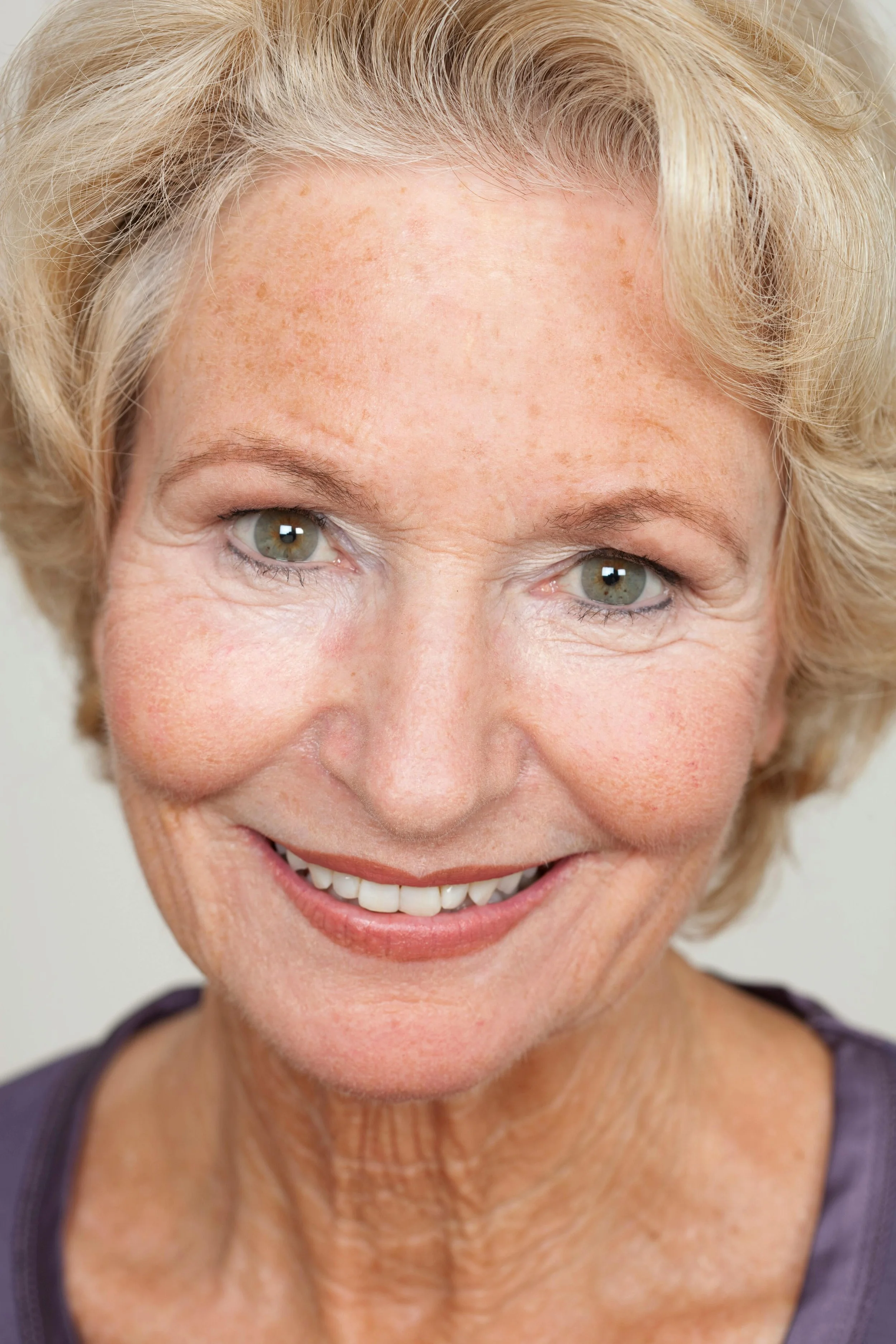Close-up of smiling elderly woman with short, curly blonde hair and green eyes