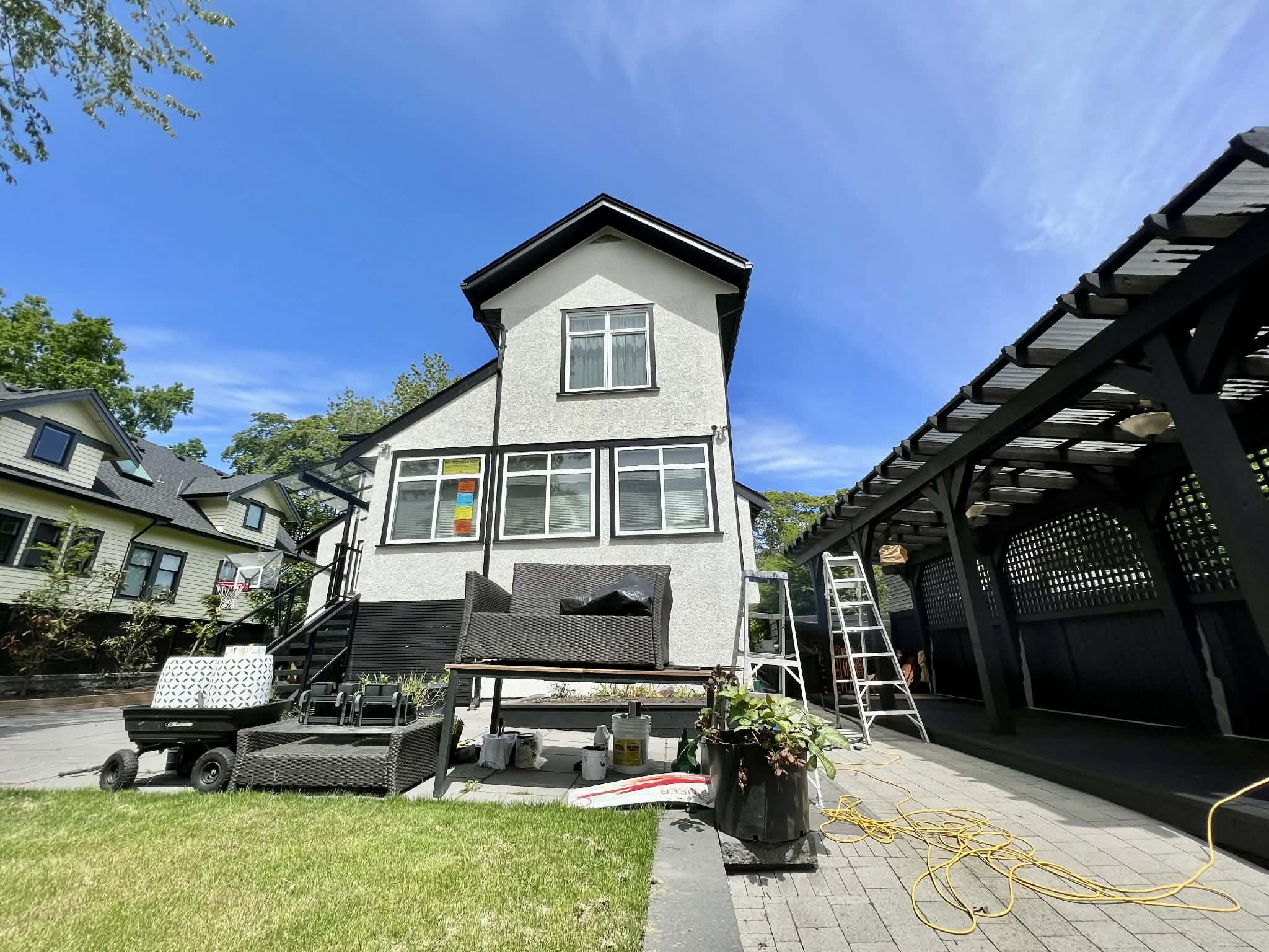 Front yard and house under repair with ladders, tools, outdoor furniture, and a sunny blue sky.