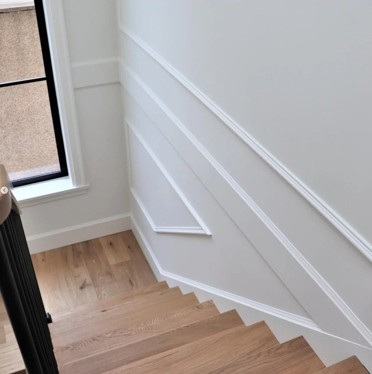 Wooden staircase next to a window with a beige wall and white crown molding