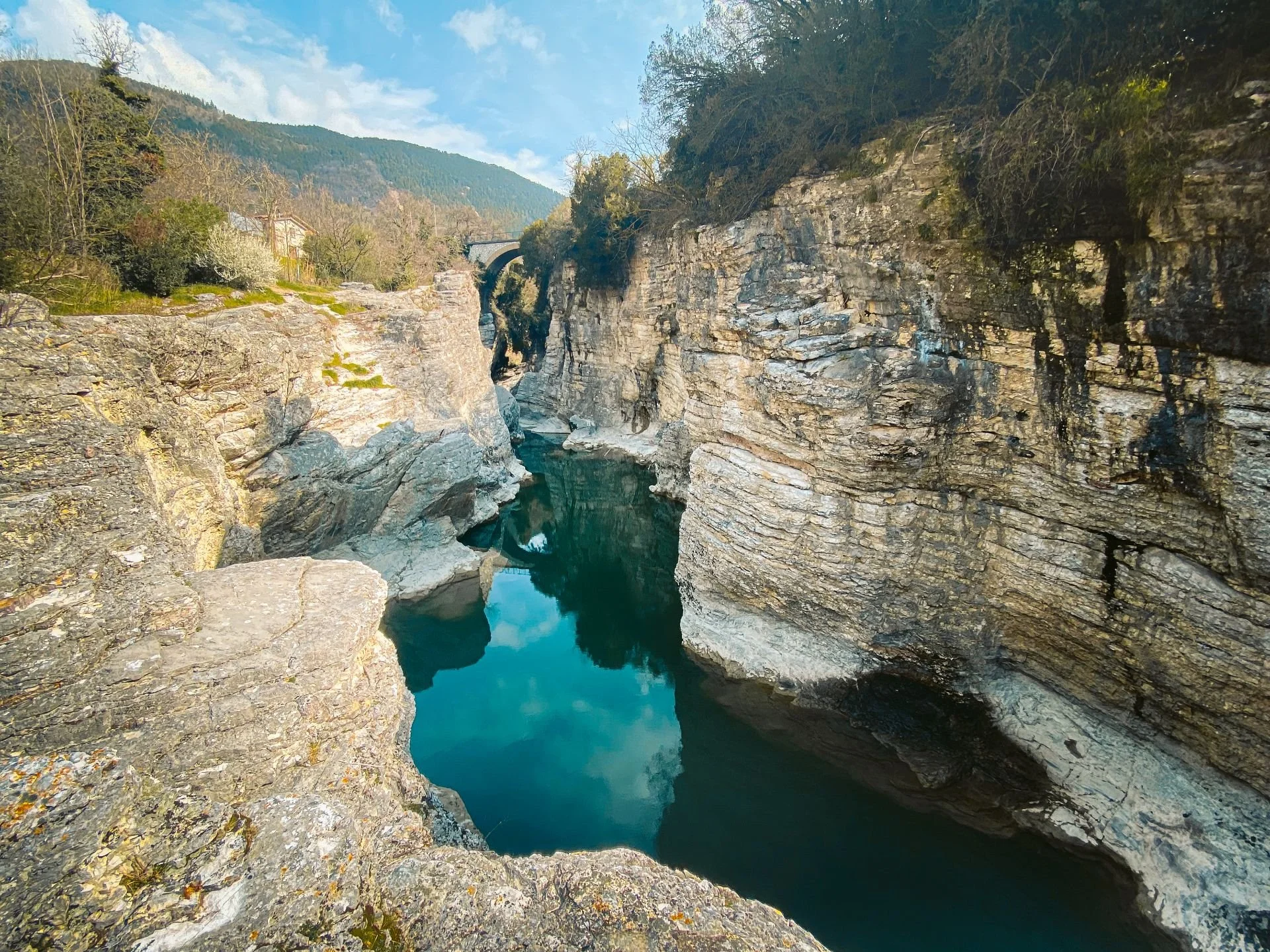 A rocky canyon with a narrow river running through it, surrounded by trees and mountains in the background.