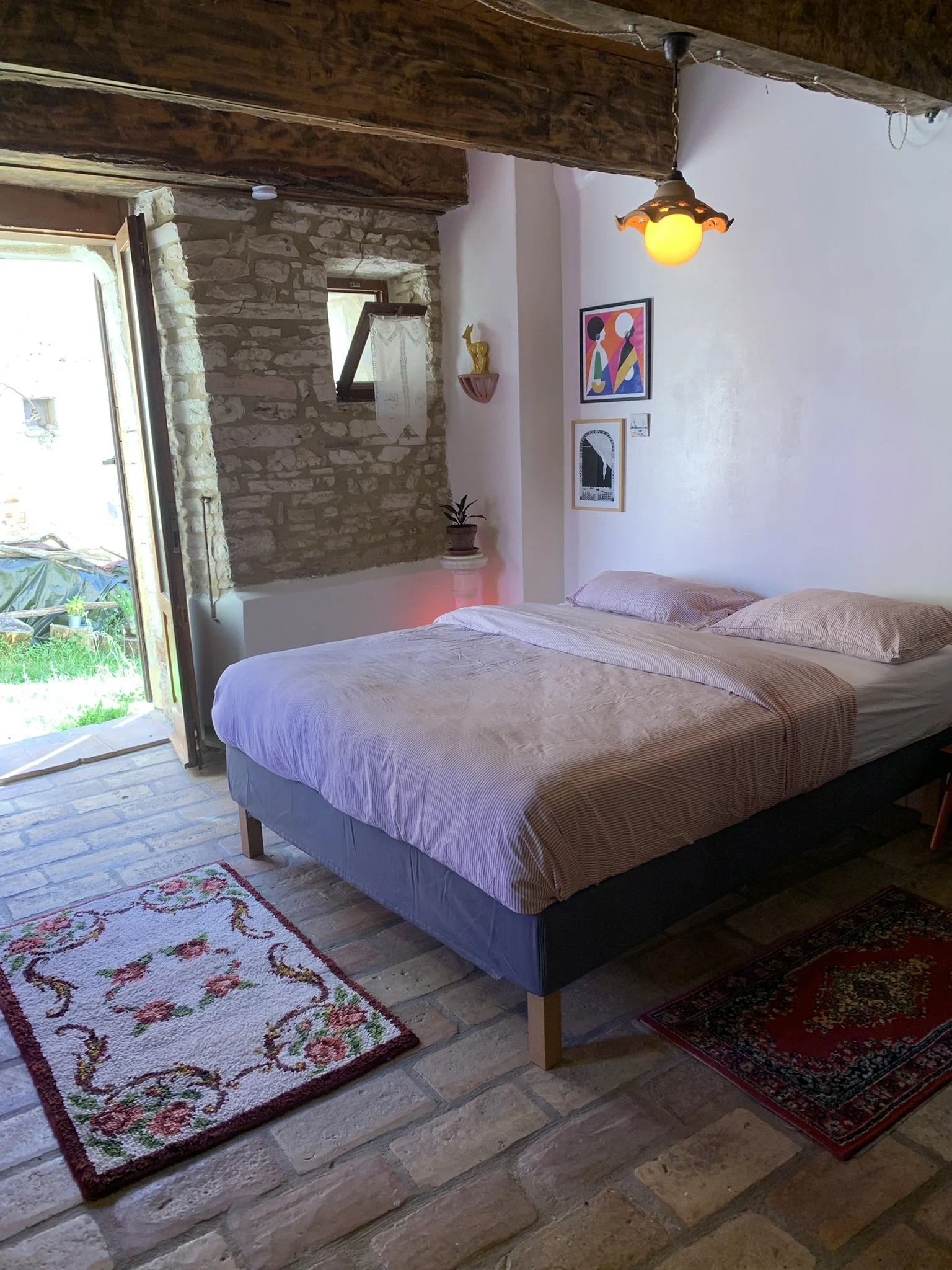 A bedroom with a bed, a patterned rug, a skylight window, a brick wall, and decorative artwork on the wall.