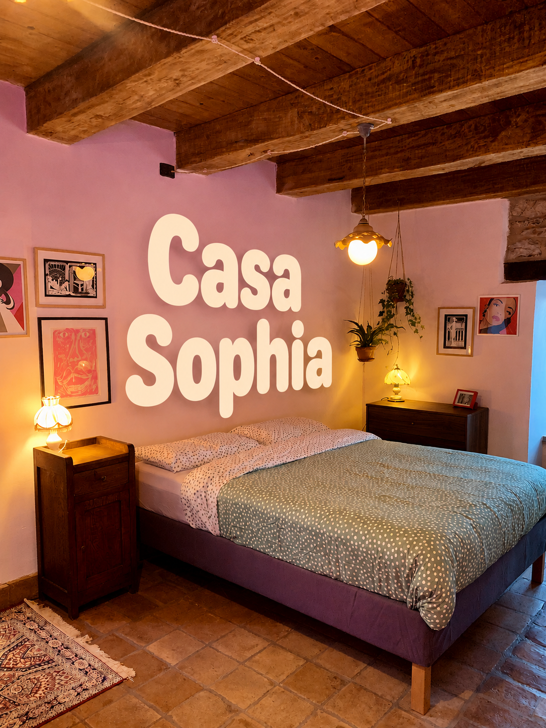 A cozy bedroom with a wooden beamed ceiling, pink walls, a bed with polka dot bedding, two bedside lamps, framed art on the walls, and hanging plants. The words 'Casa Sophia' are projected on the wall.