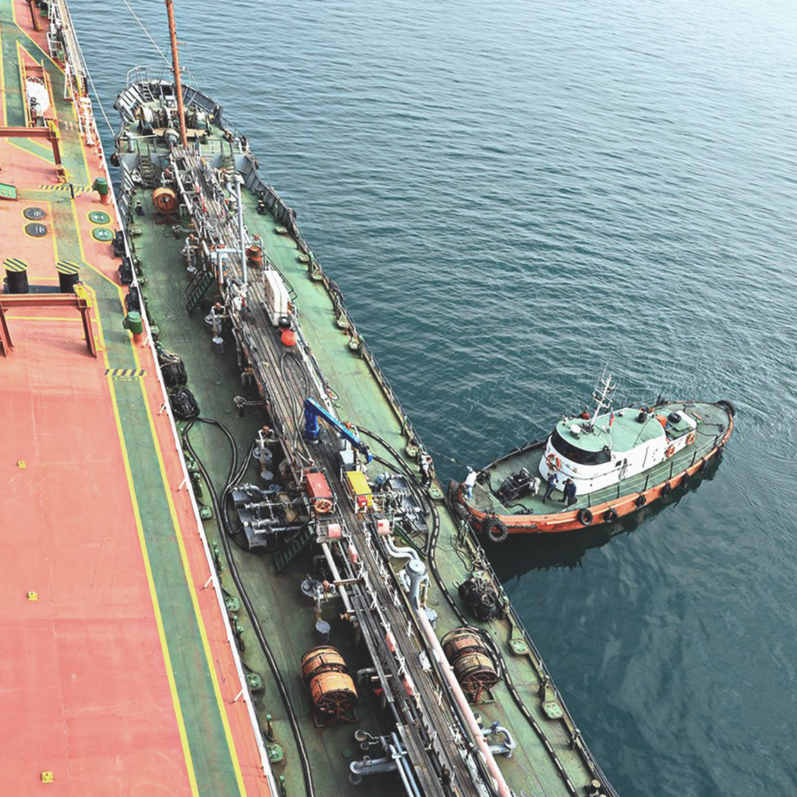 View of a docked tanker ship with an emergency boat nearby, showing maritime equipment and personnel.