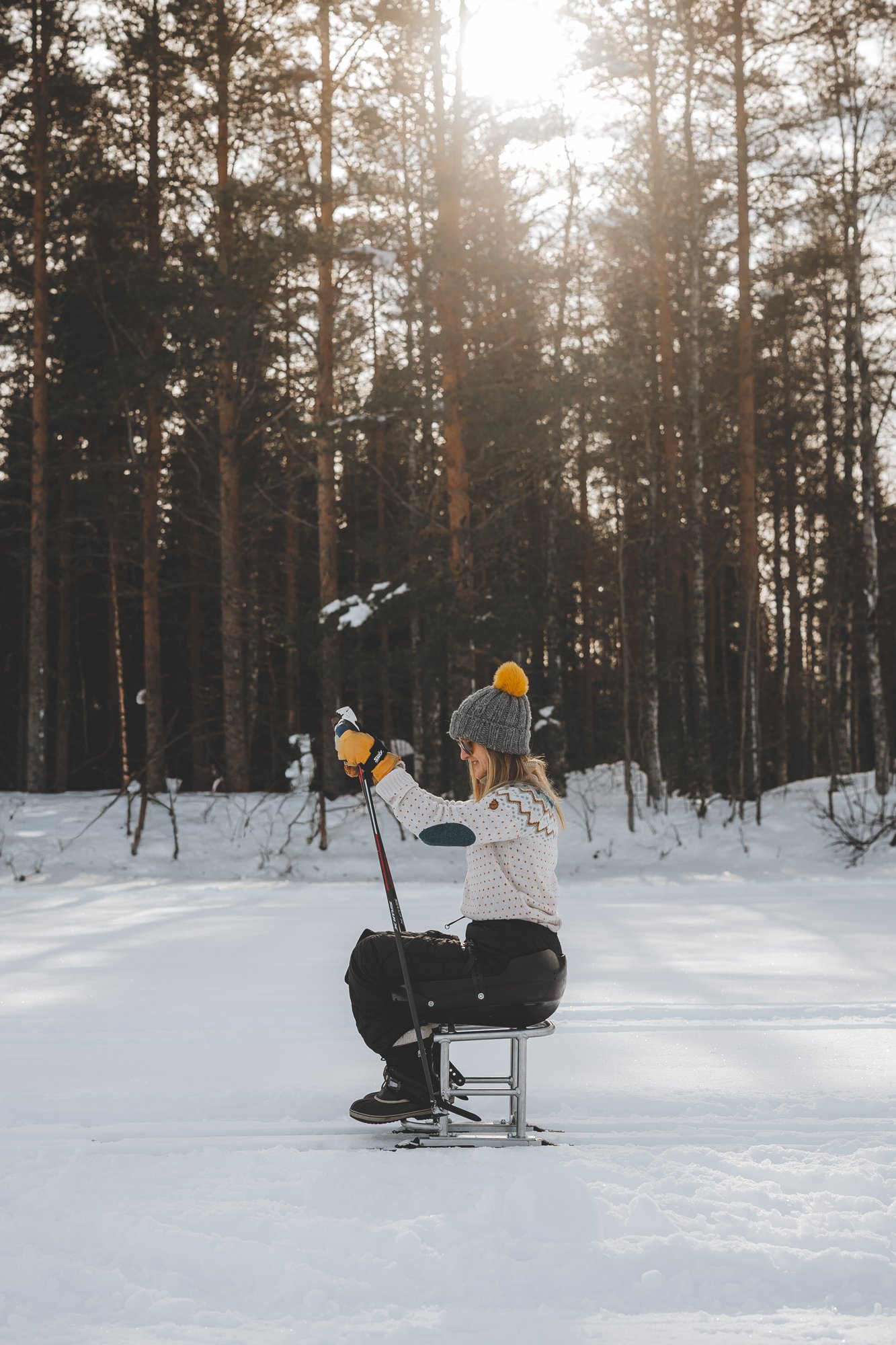 Nainen hiihtää suksipyörätuolilla ja työntää vauhtia sauvoilla, kuvattuna sivusta.