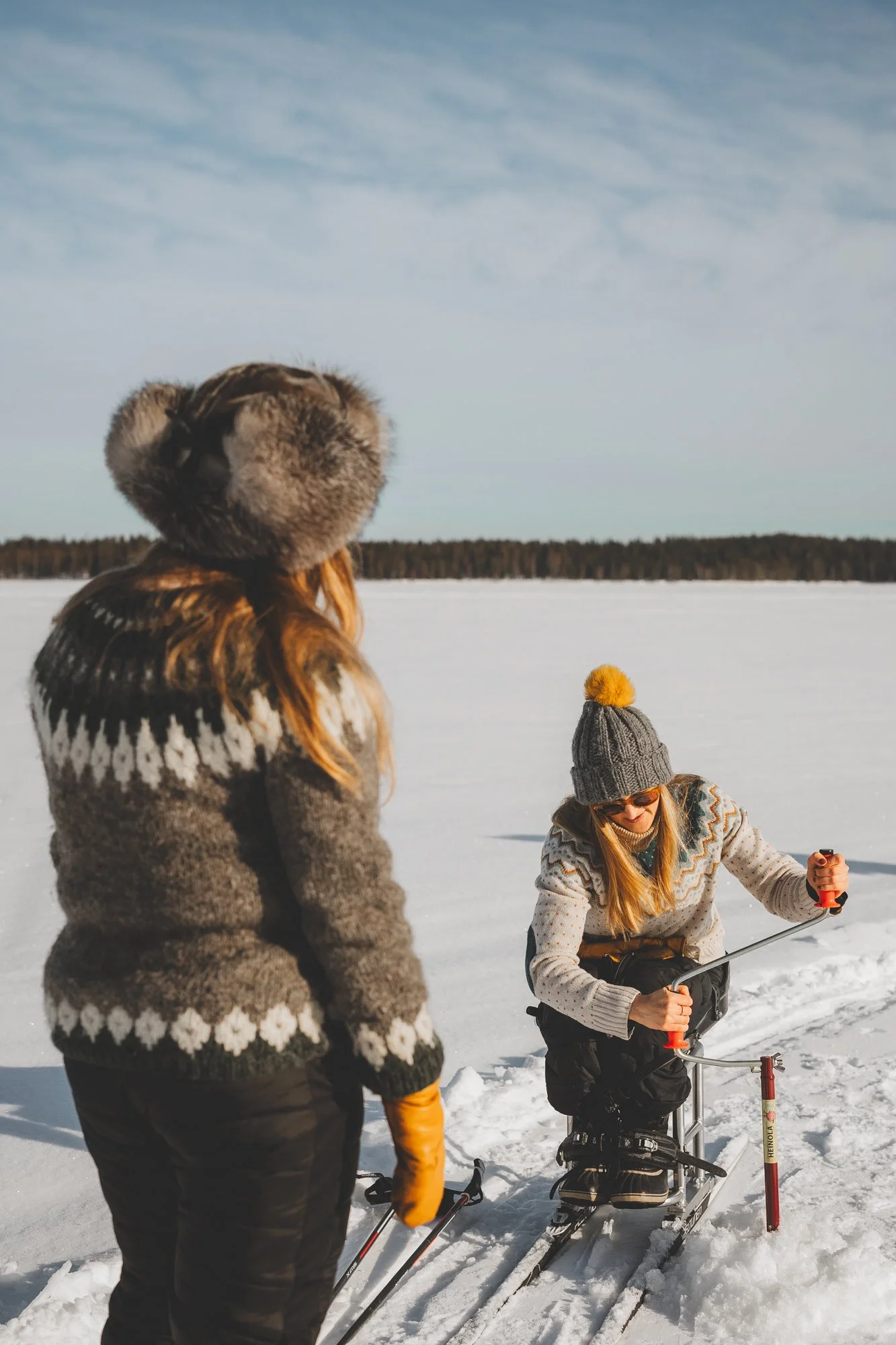 Naiset pilkkivät yhdessä järven jäällä. Pyörätuolissa istuva nainen kairaa jäähän reikää.