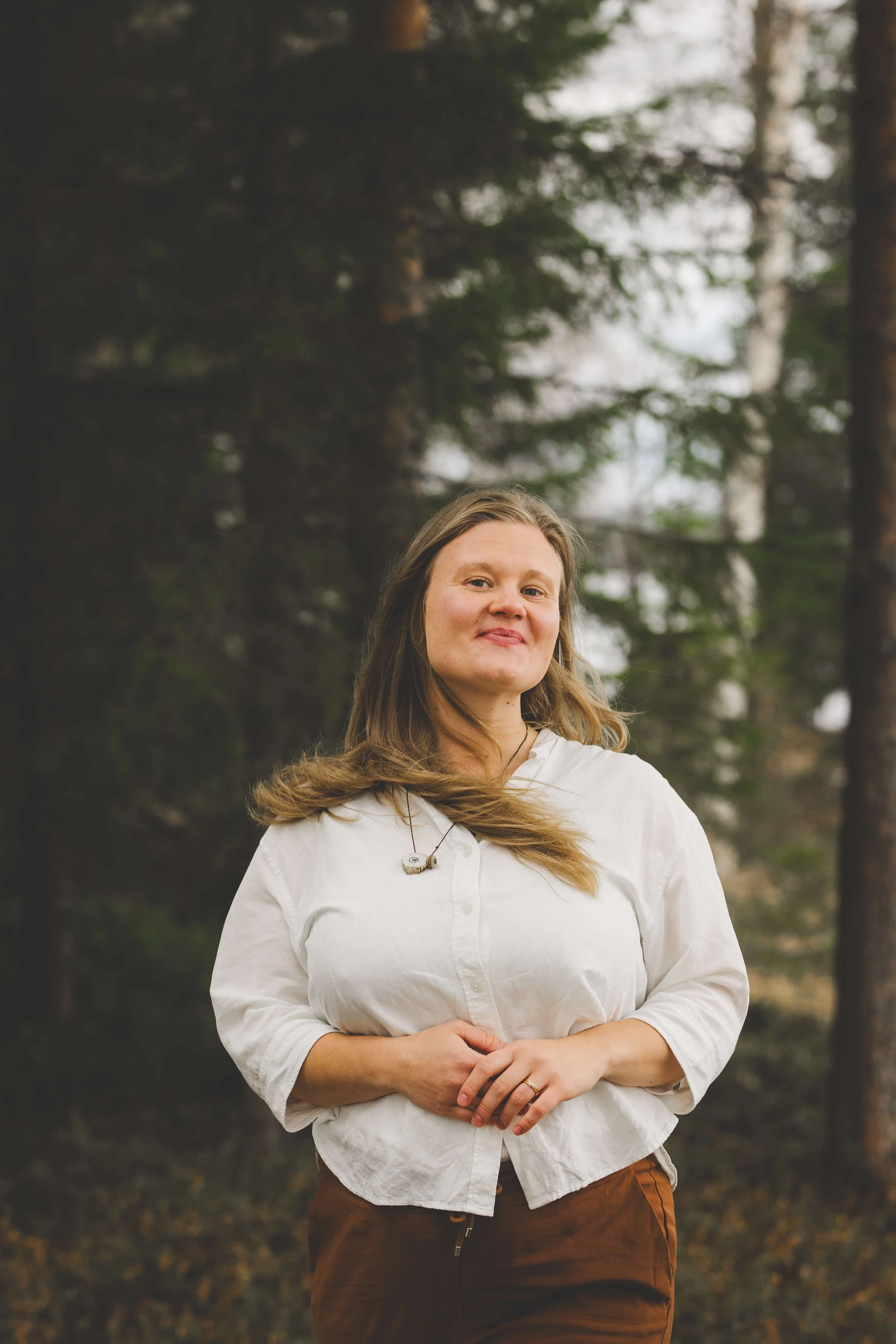 Kristiina seisoo metsässä ja hymyilee, hiukset tuulessa heiluen.