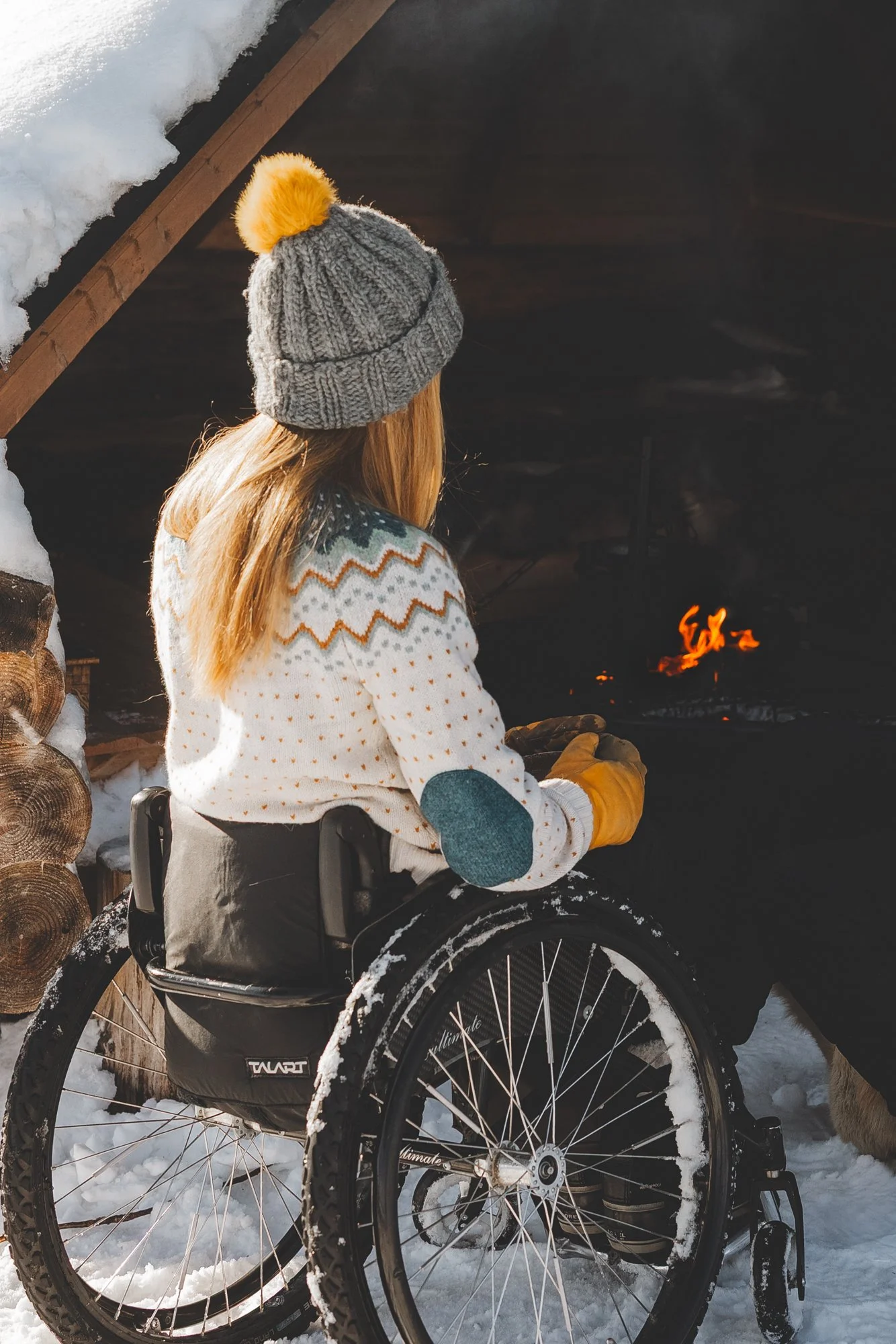 Nainen istuu pyörätuolissa laavulla kädessään kuksa.