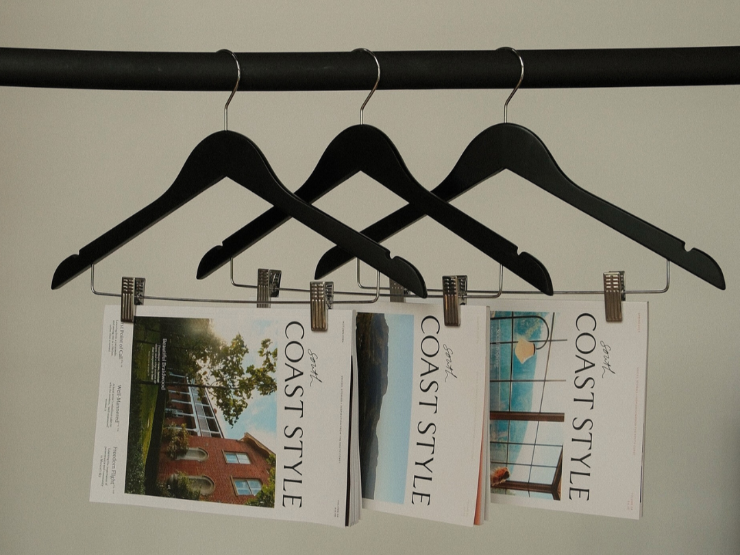 Three magazines hanging on black hangers, secured with clips, showing different outdoor scenery and architectural designs on the covers.