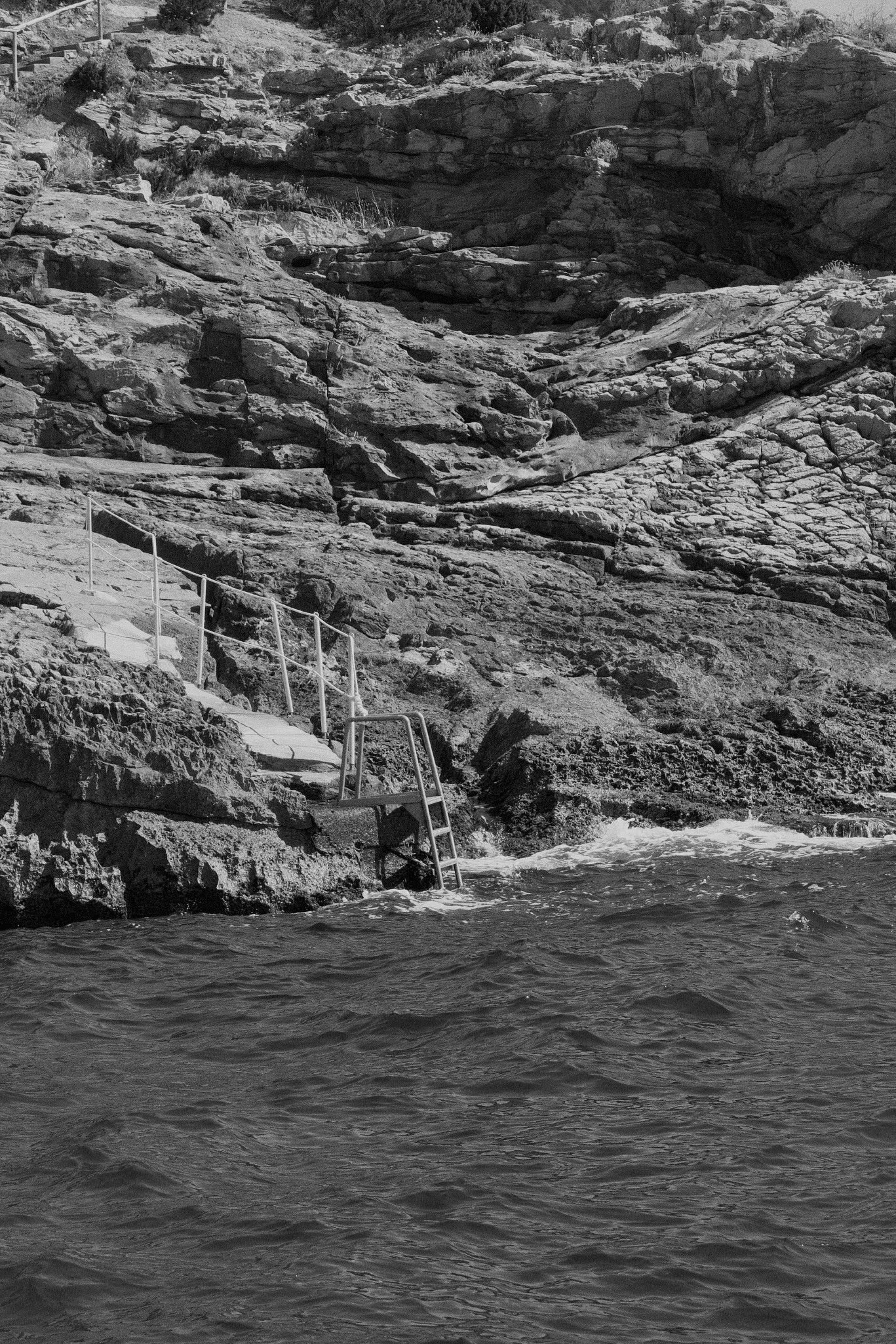 A rocky shoreline with stairs leading down to the water, surrounded by large rocks and water at the bottom of the image.