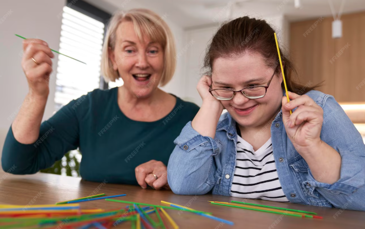 Older woman and young girl playing with colorful spaghetti strands at a table.