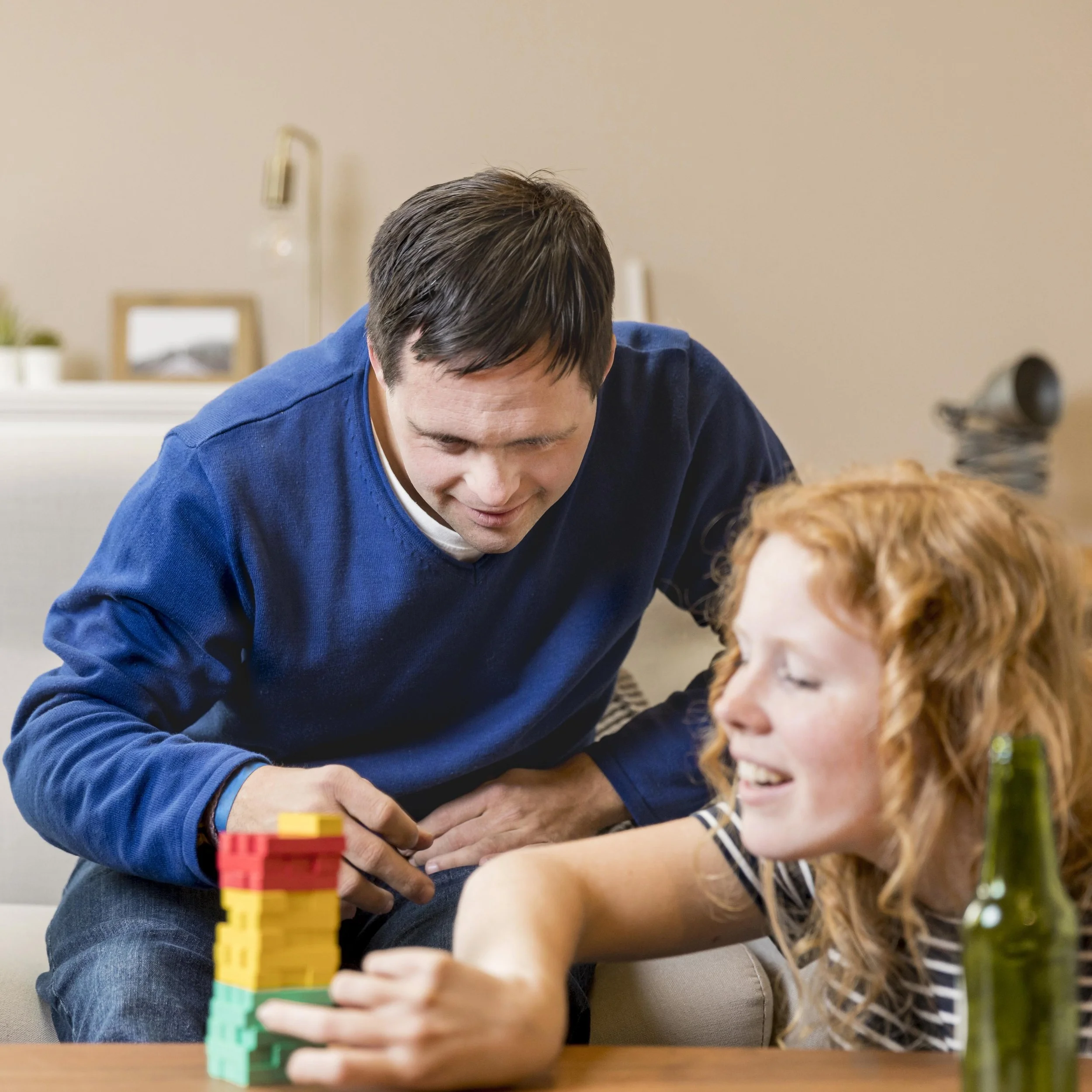 A man and a woman playing a stacking game with colorful blocks at home.