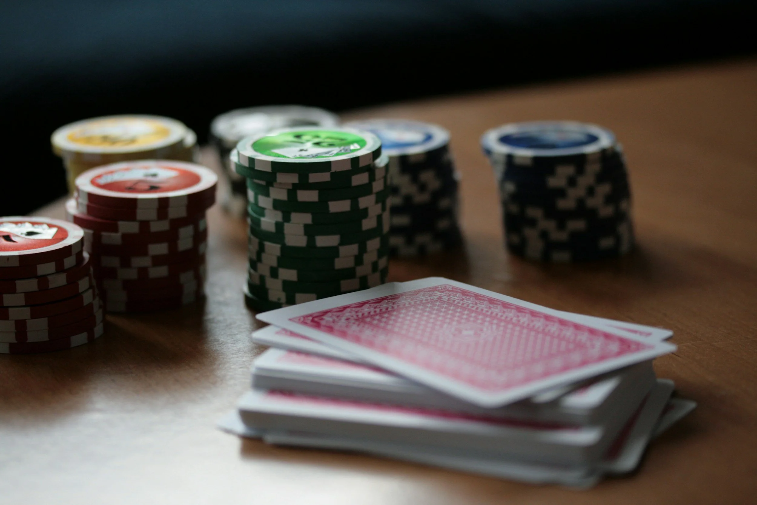Poker chips in various colors and a deck of playing cards on a wooden table.