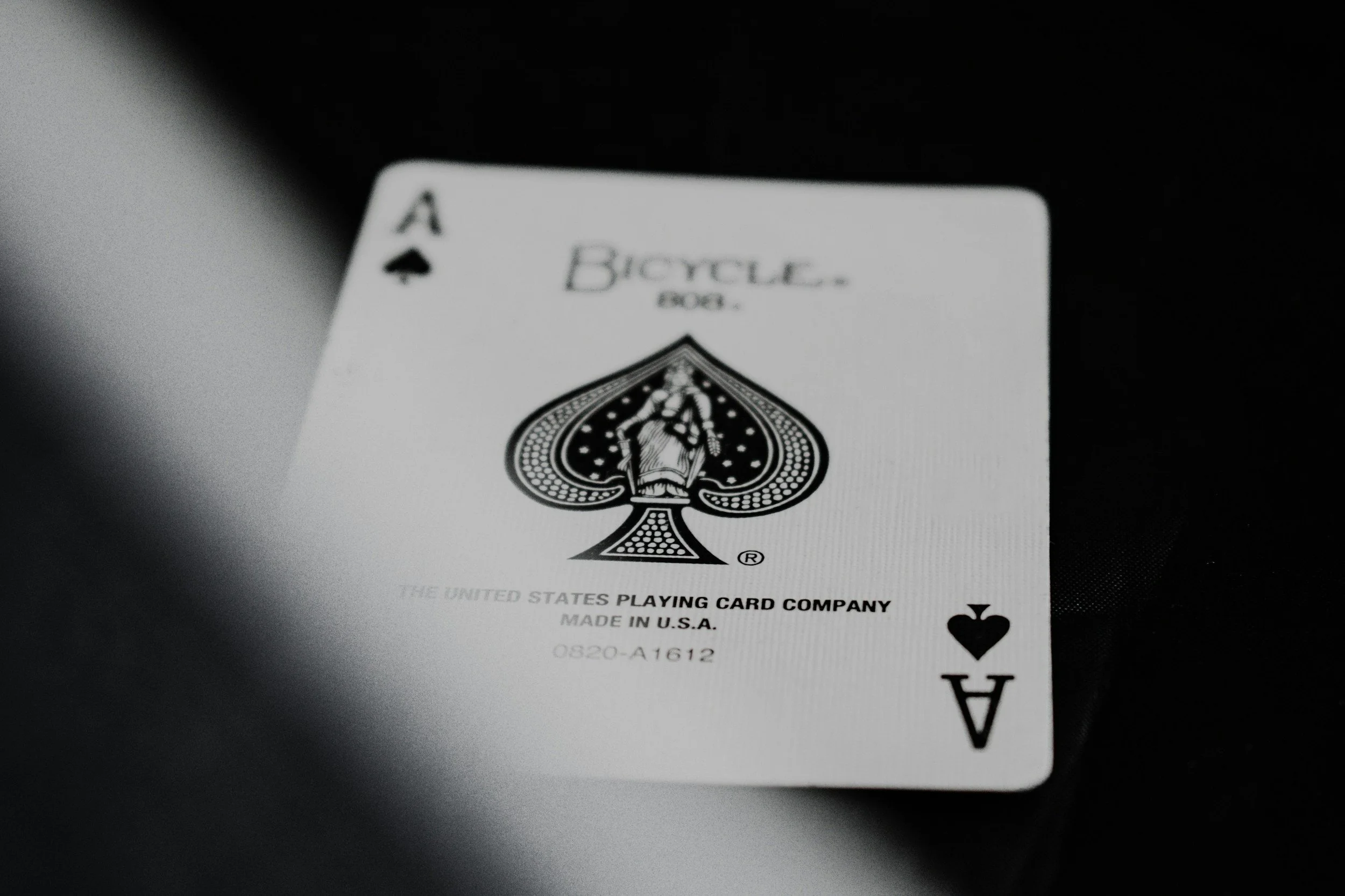 Black and white photograph of an Ace of Spades playing card with a spade symbol and a design in the center, labeled 'Bicycle' and 'THE UNITED STATES PLAYING CARD COMPANY'.