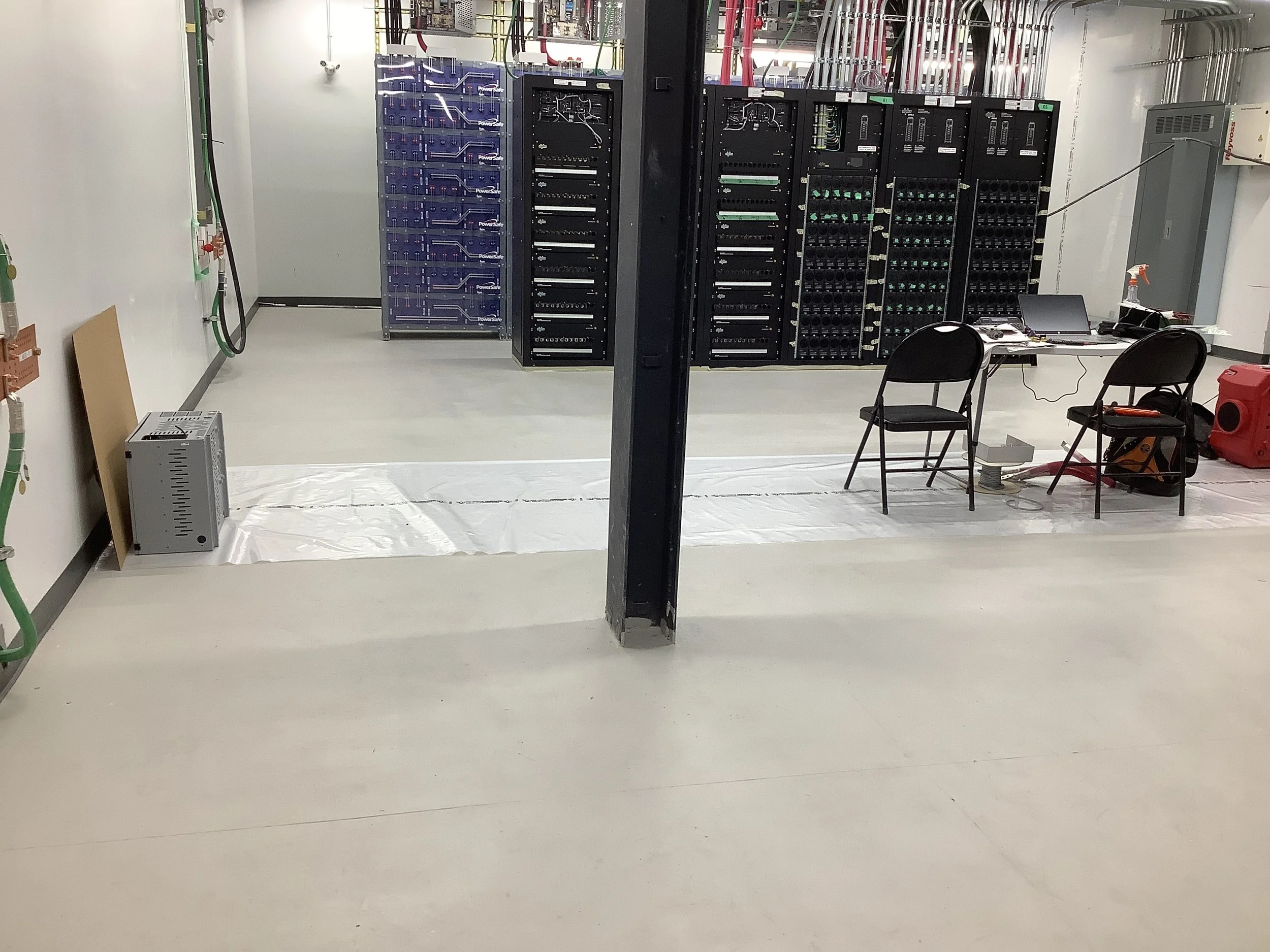 Room with server racks, a table with chairs, and electronic equipment, indicating a data center or technical workspace.