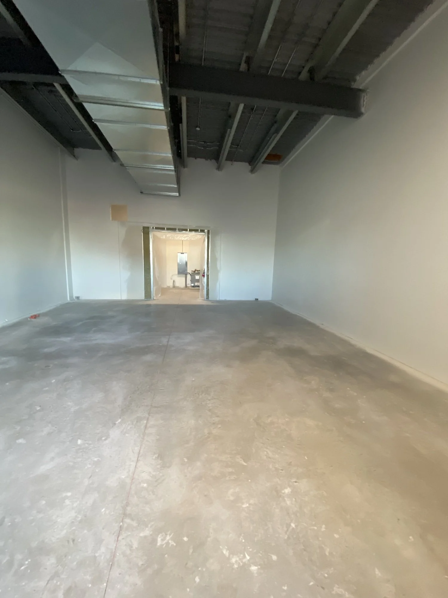 Empty room under construction with exposed ceiling and unfinished concrete floor, doorway at end leading to another space, hall or room.