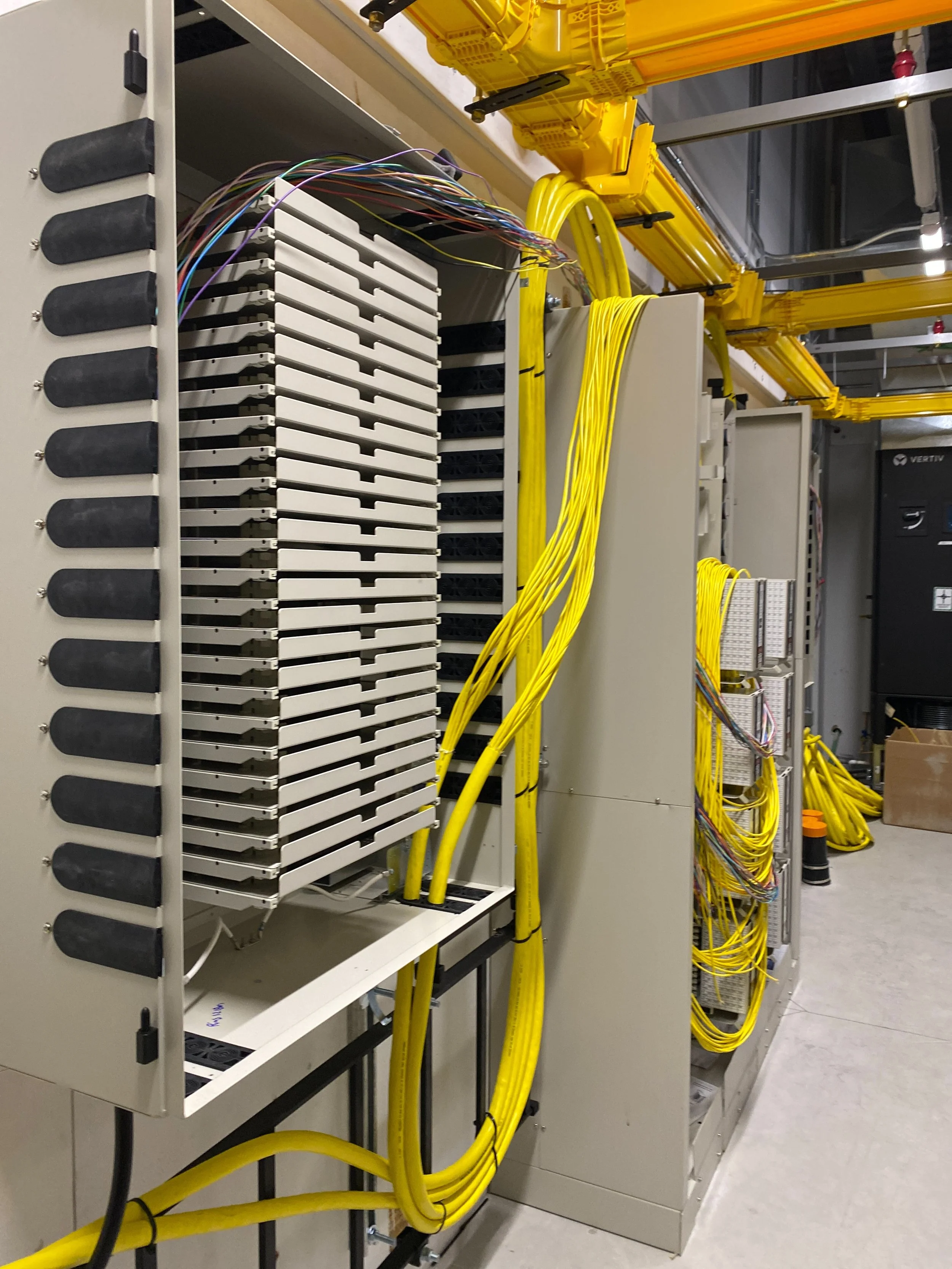 Network equipment with multiple yellow cables connected to a server rack in a data center.