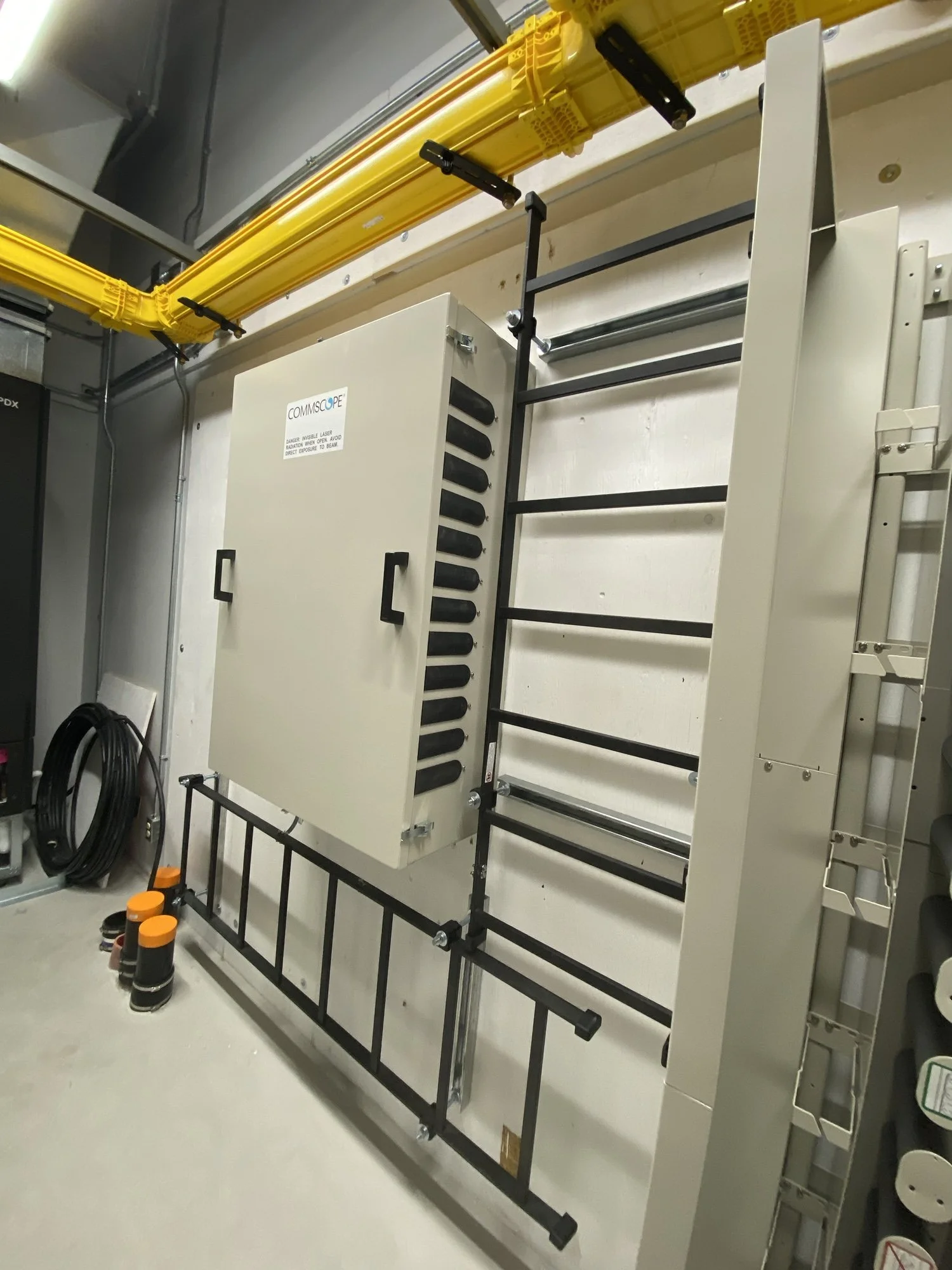 Electrical control panel cabinet mounted on a wall with black metal ladder and yellow cables above.