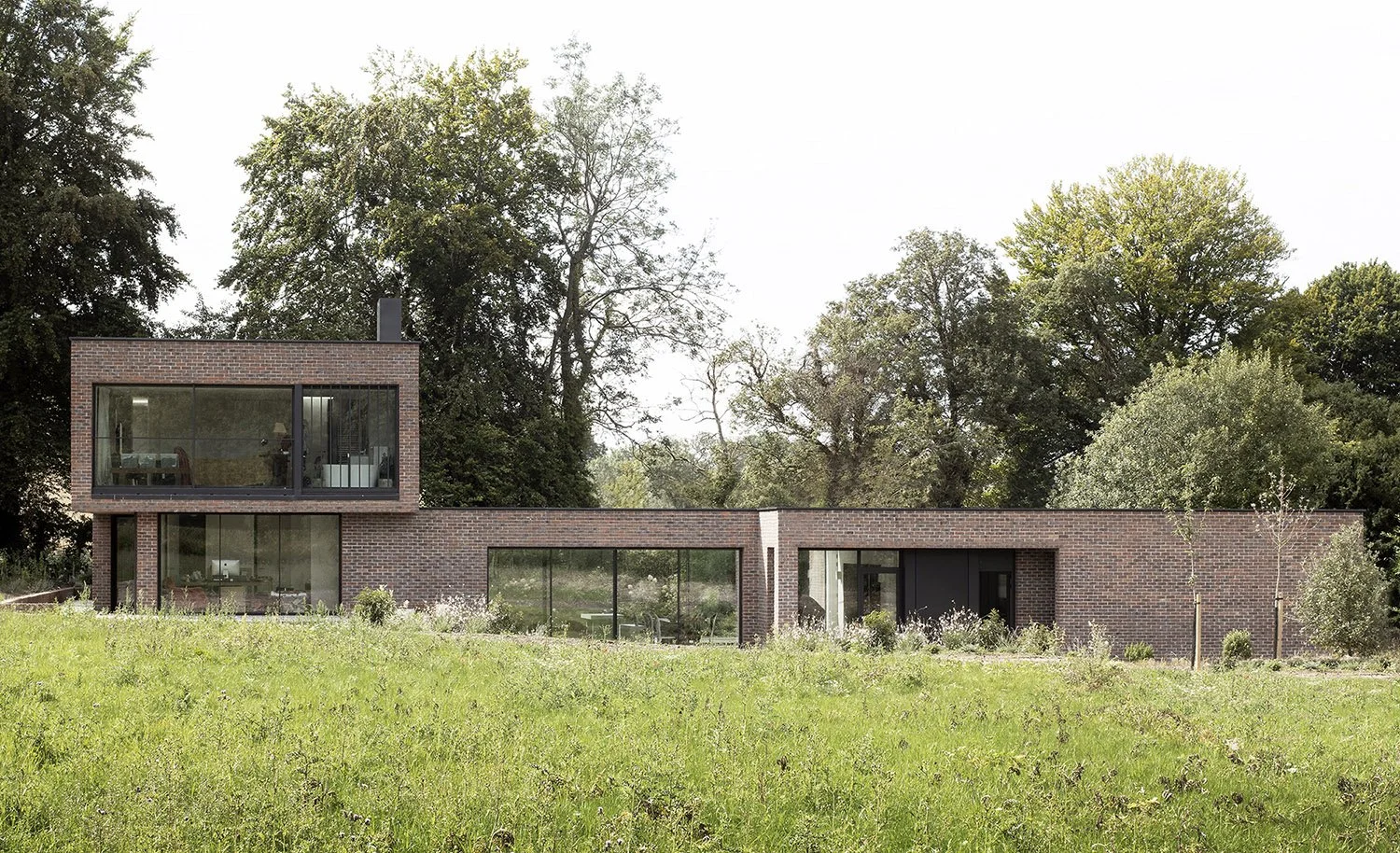 Modern brick house with large glass windows on a grassy lawn, surrounded by trees