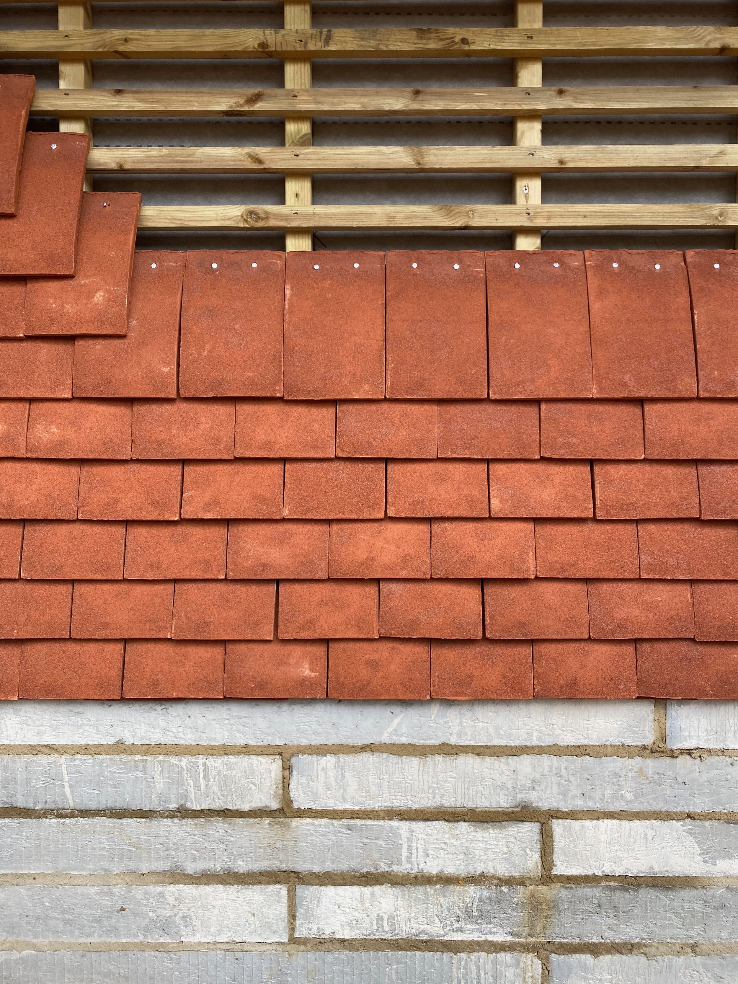 Close-up view of a construction site showing a partially completed wall with wooden framing, red roofing tiles, and white bricks.