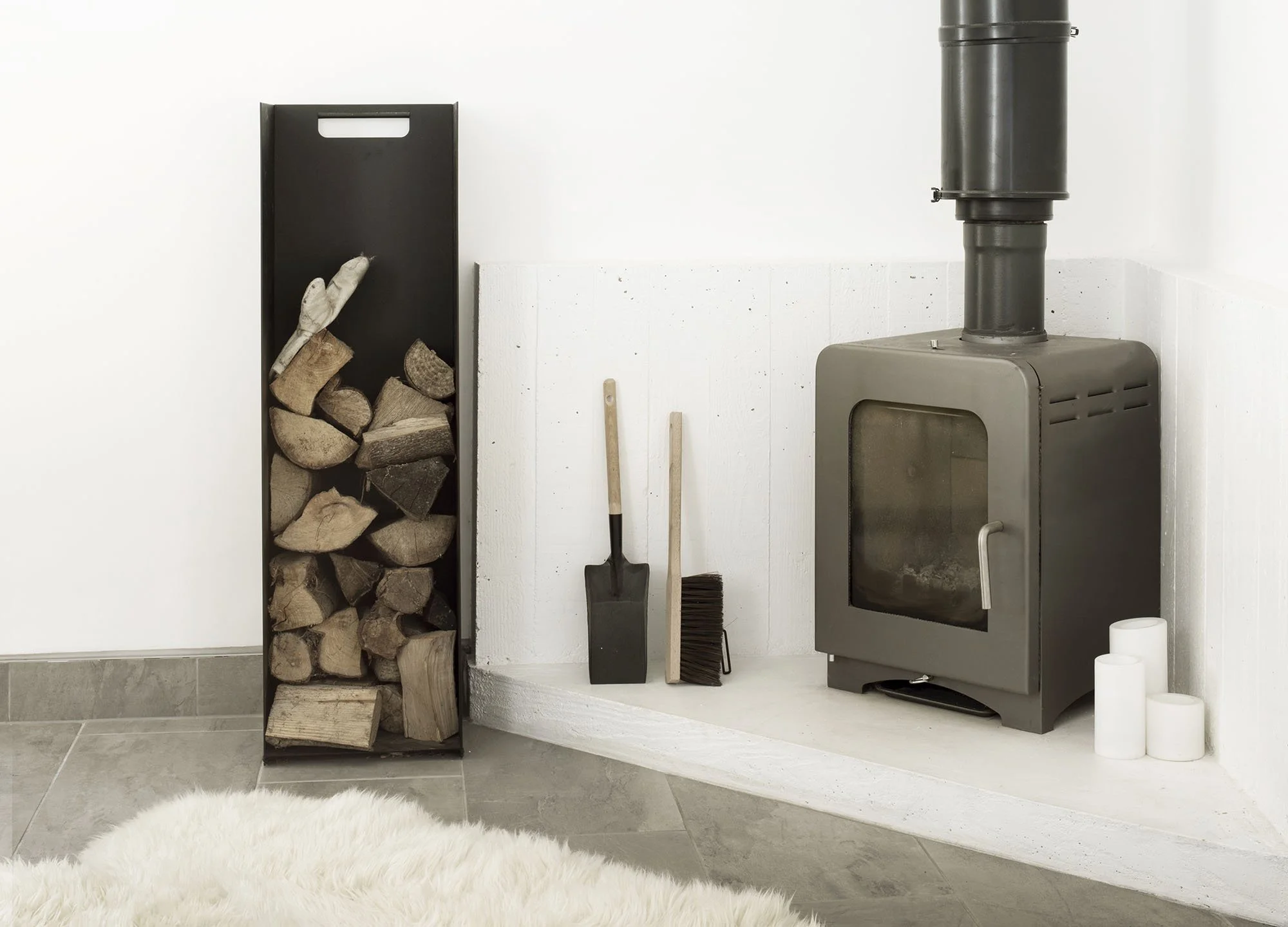 Wood log holder, fireplace tools including a shovel, broom, and candles in a living room corner.