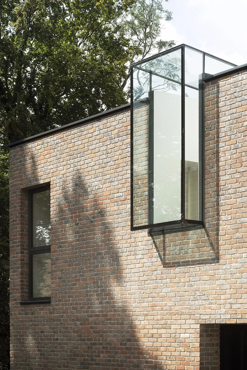 Paul Cashin Architects : Close-up of a modern brick building with large glass window projecting outward, surrounded by trees.