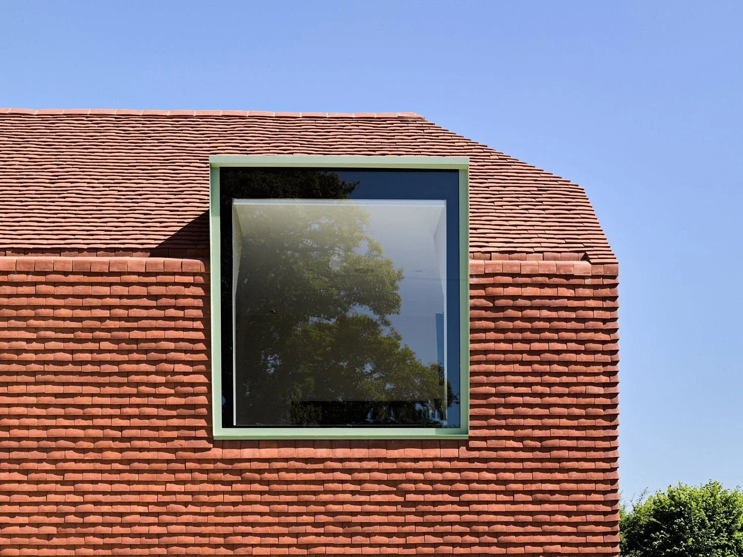 Paul Cashin Architects : Close-up of a building's facade with red brick siding and a large square window reflecting a tree and blue sky.