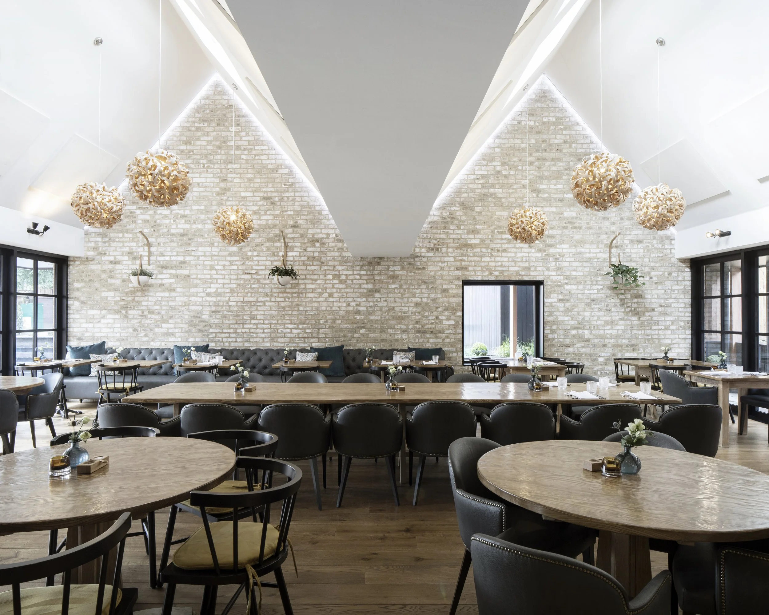 Interior of a modern restaurant with white brick walls, hanging pendant lights, and wooden tables with black and beige chairs.