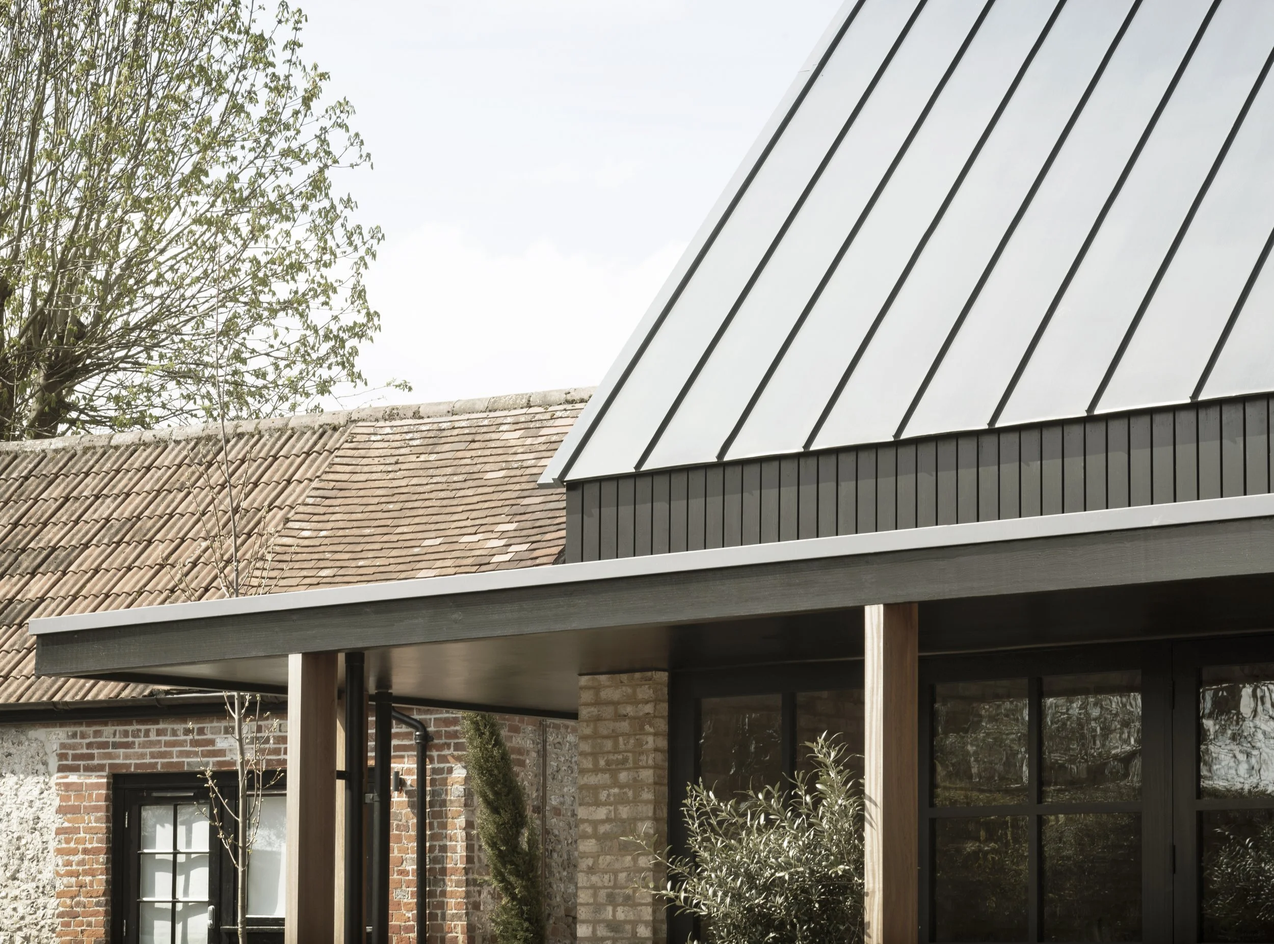 Close-up of a modern house with a brick wall, black window frames, and a metal roof with vertical panels.