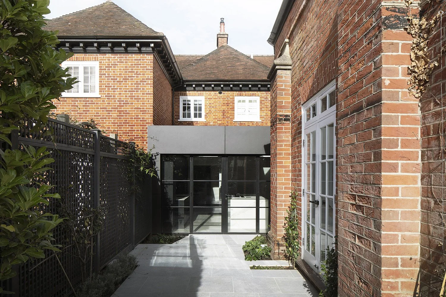 Rear view of a brick house with black metal fencing, a glass door, and surrounding greenery.