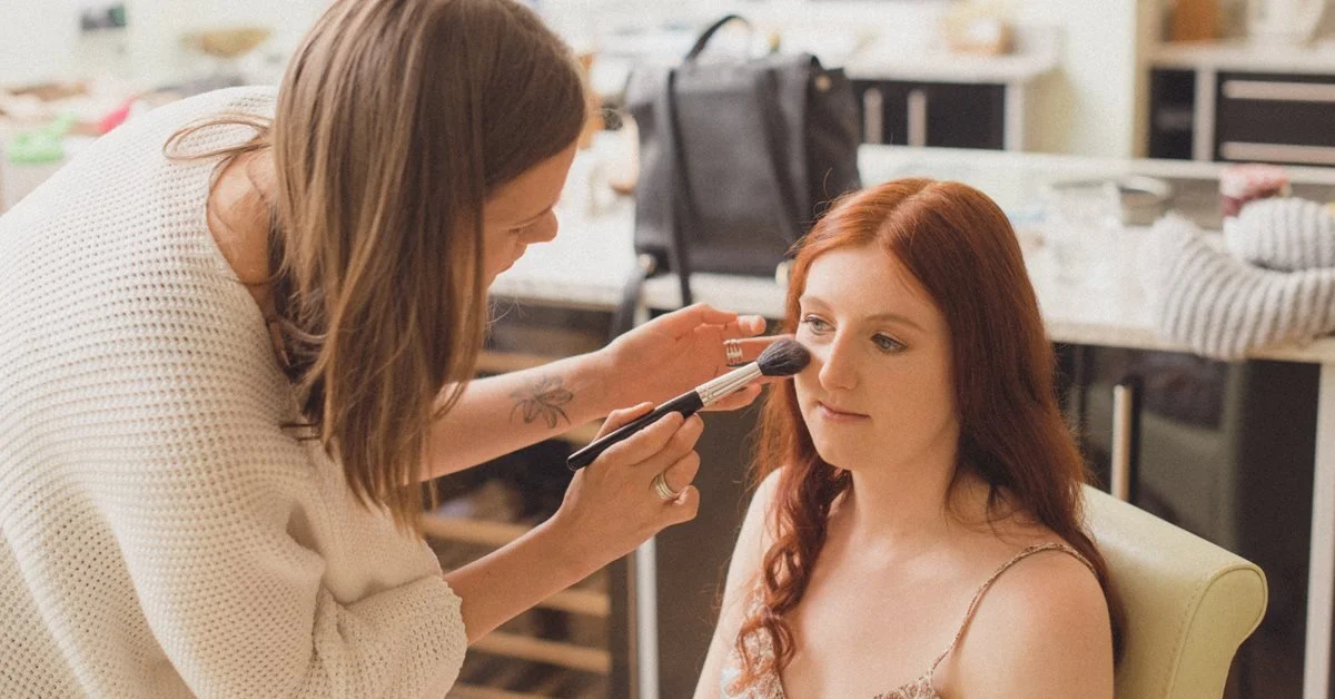 Makeup artist applying makeup to a woman sitting in a chair in a dressing room.