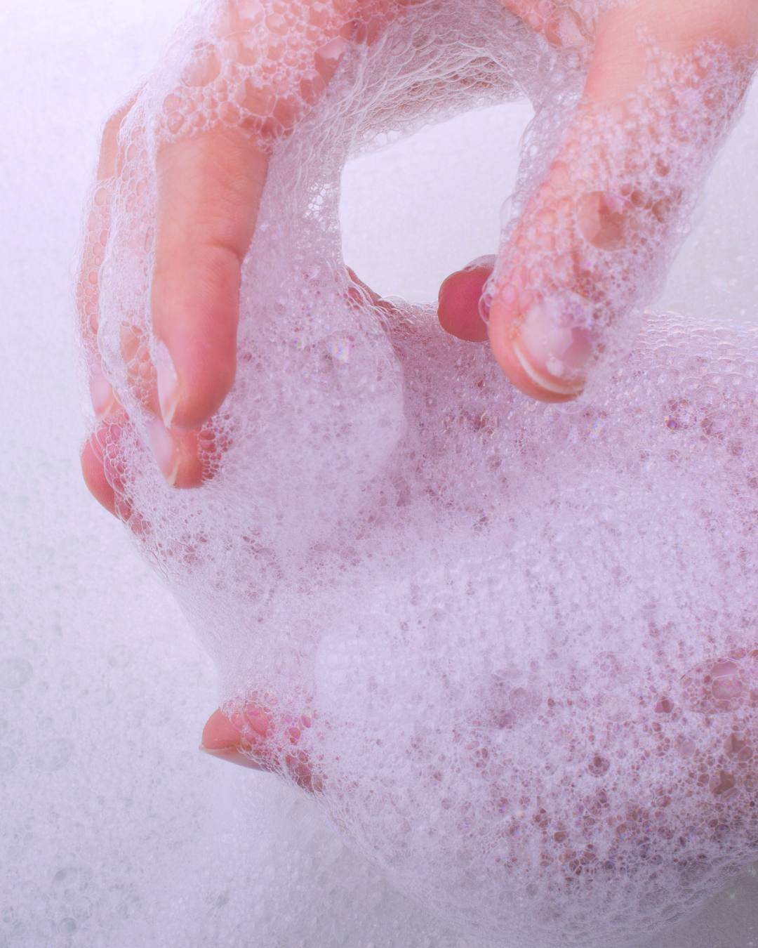 Close-up of a person's hand with soap lather forming bubbles during hand washing or bathing.