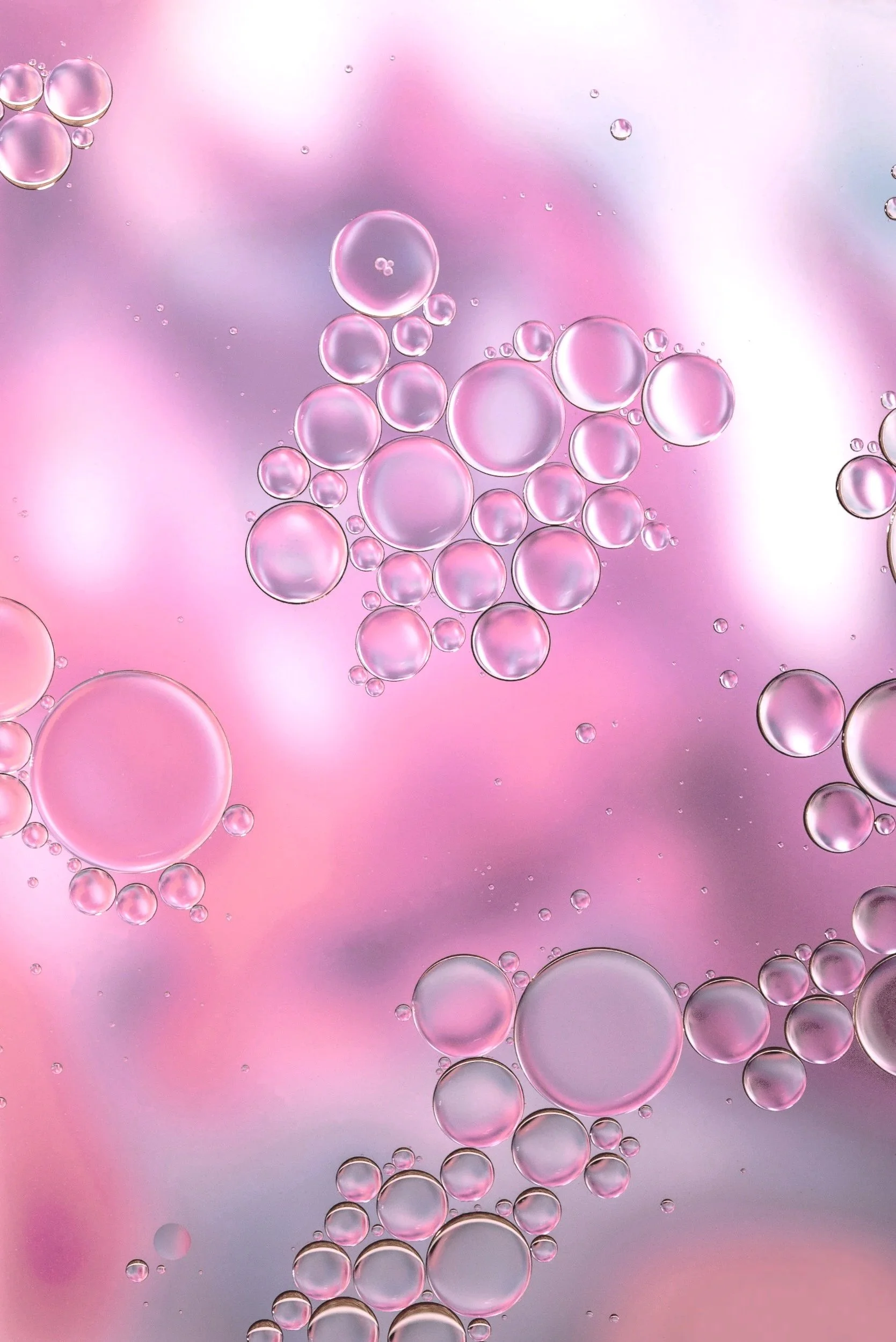 Close-up of pink and clear bubbles floating in water with a soft pink and purple background.
