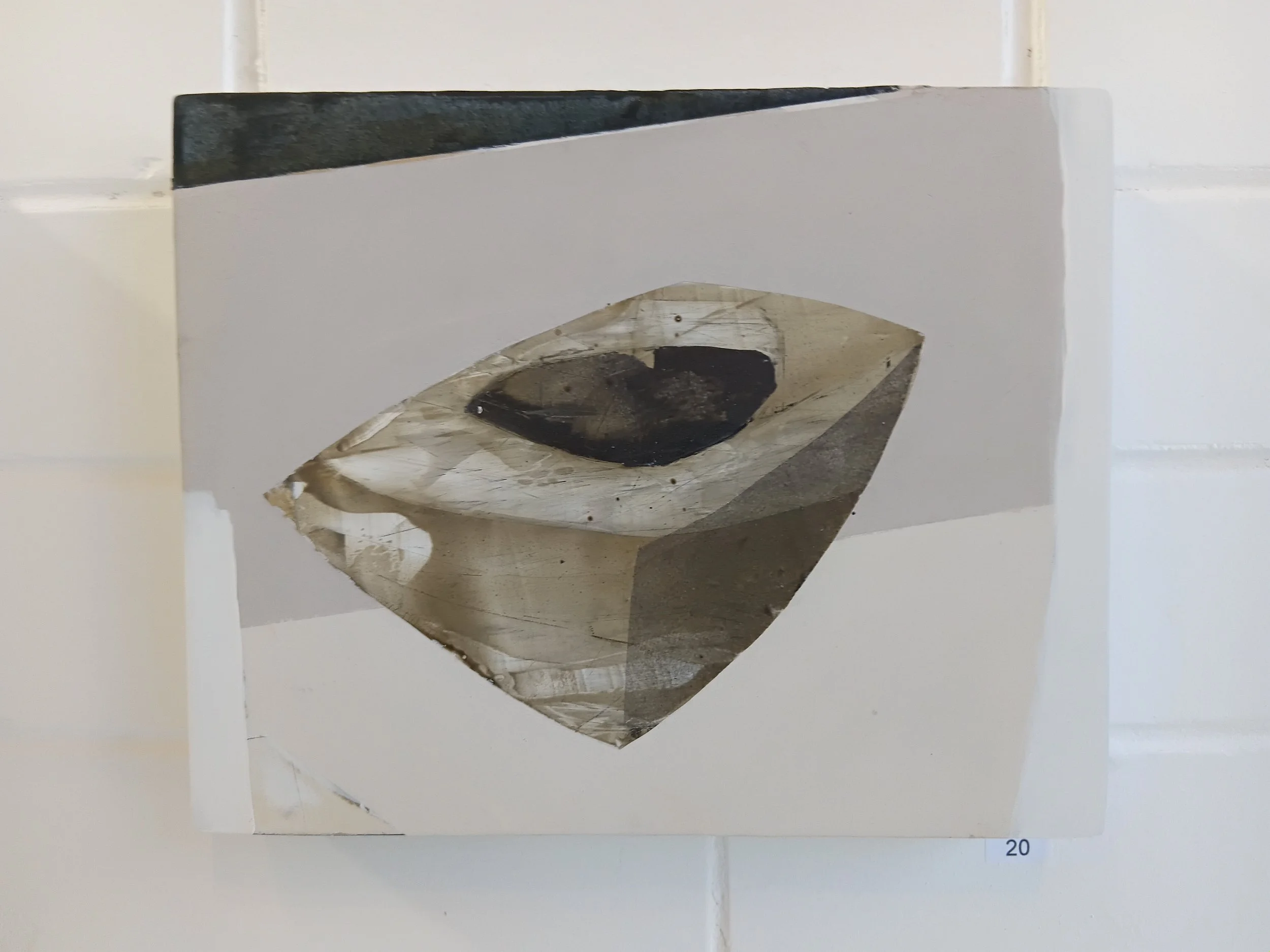 Abstract art piece with a geometric shape and a dark central spot, mounted on a white wall.