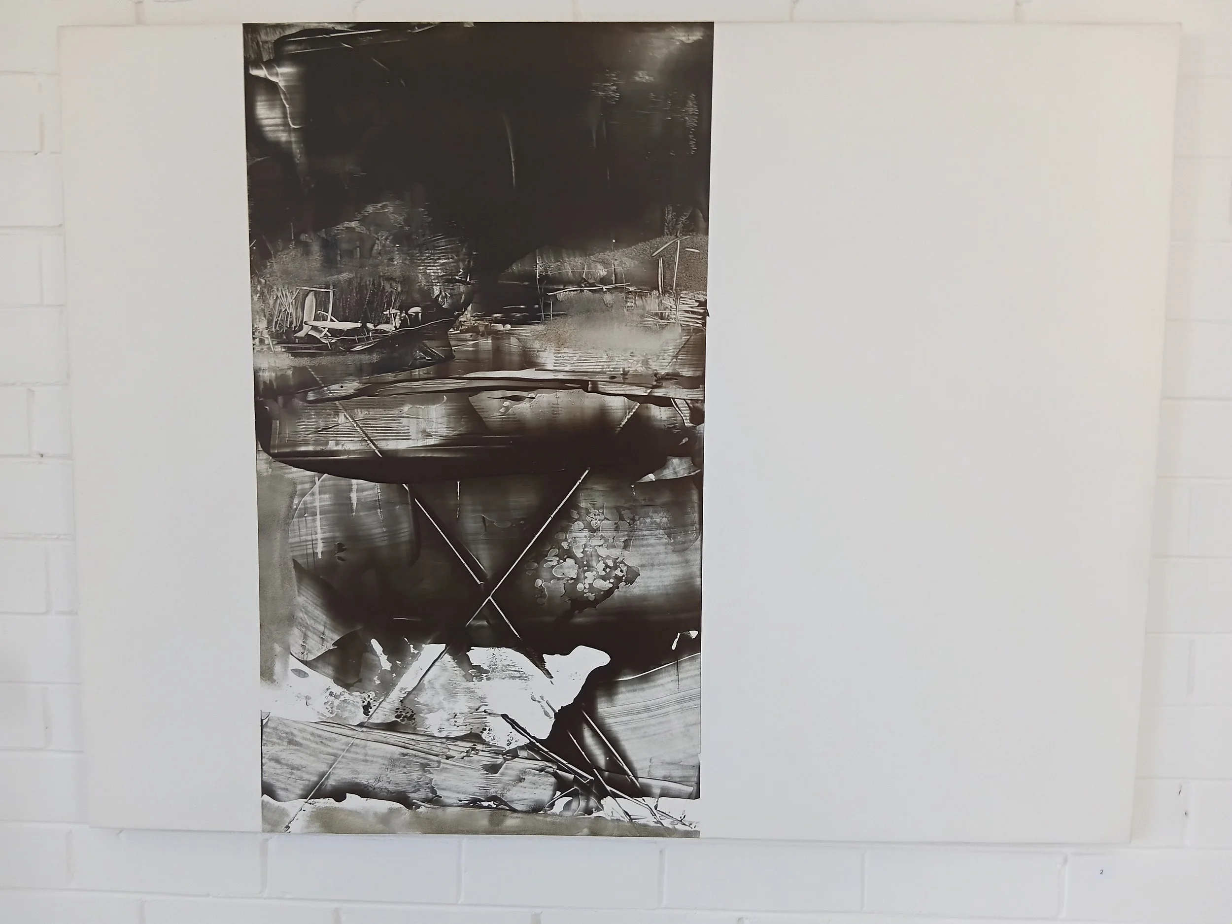 Black and white abstract painting with various shapes and textures, mounted on a white brick wall.