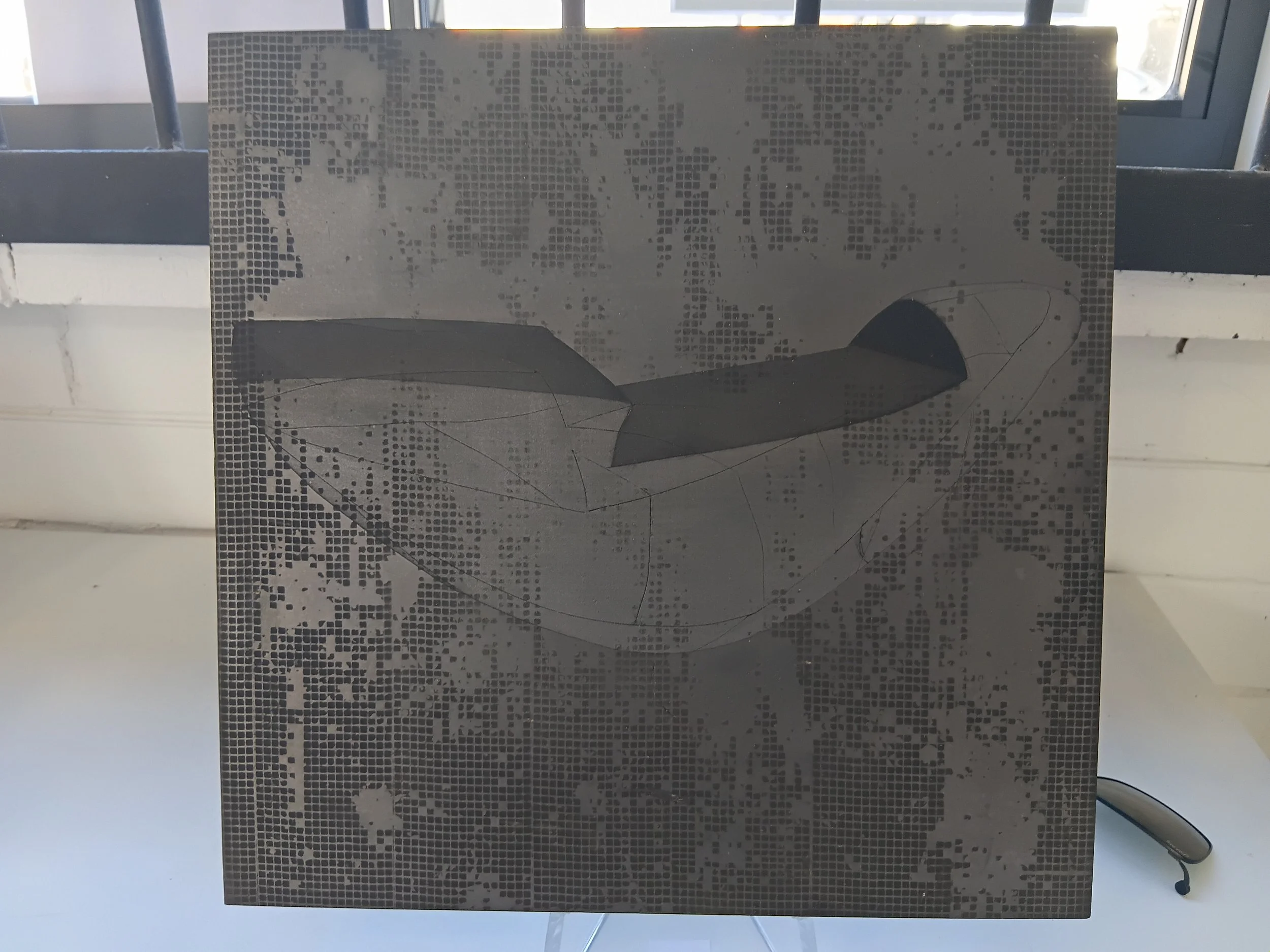 A pixelated artwork or poster featuring a abstract shape with a shadow, mounted on a stand near a window.