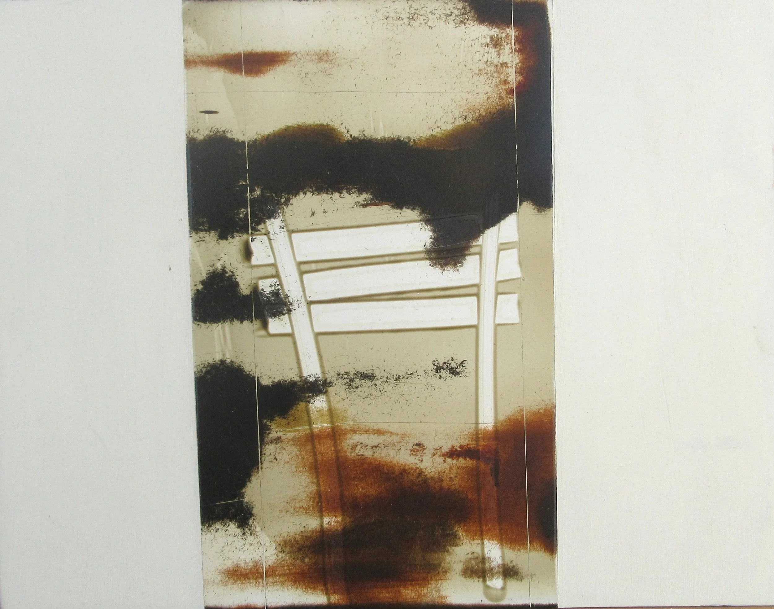 A picture of a white chair with a large, dark stain or pattern on the seat and backrest, reflected in a mirror or surface with some reddish-brown discoloration around the edges.
